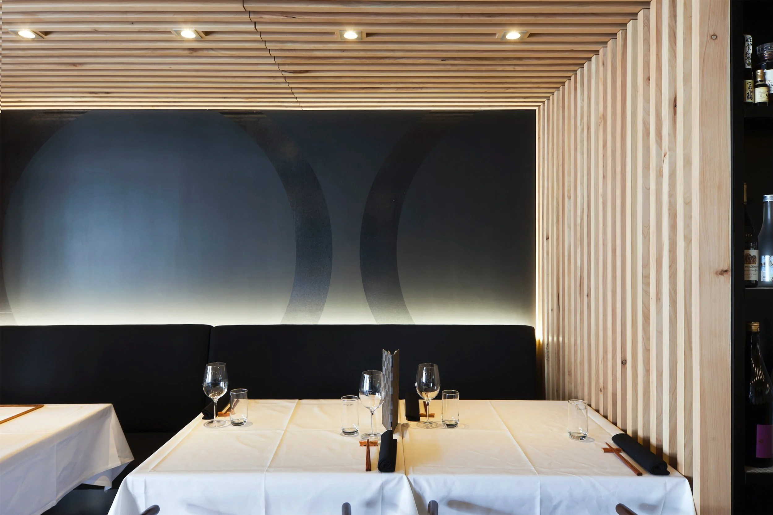 A banquette table set for service, timber battens turning up into the ceiling