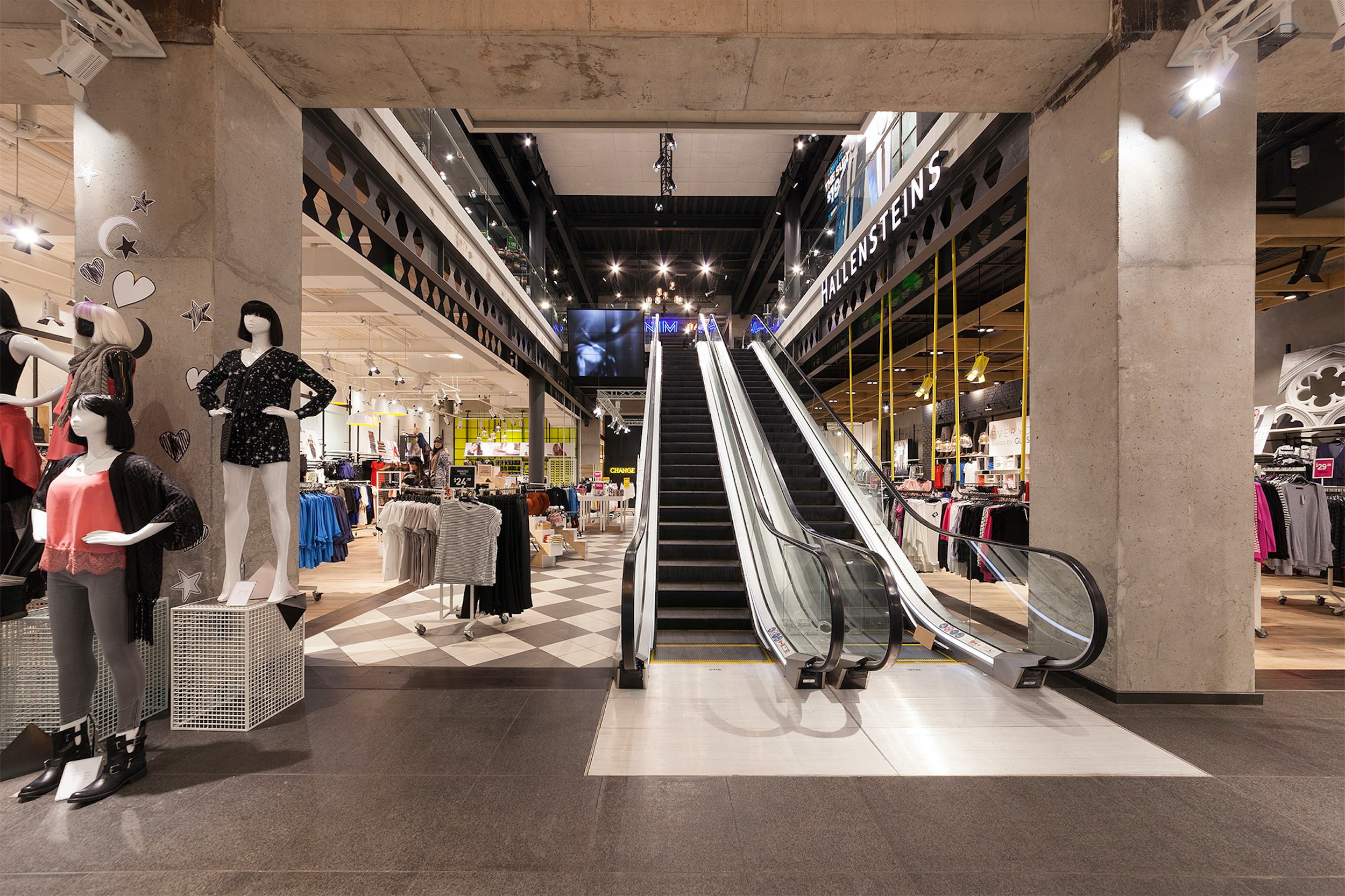 Interior of a clothing store with mannequins, clothing racks, and escalators.