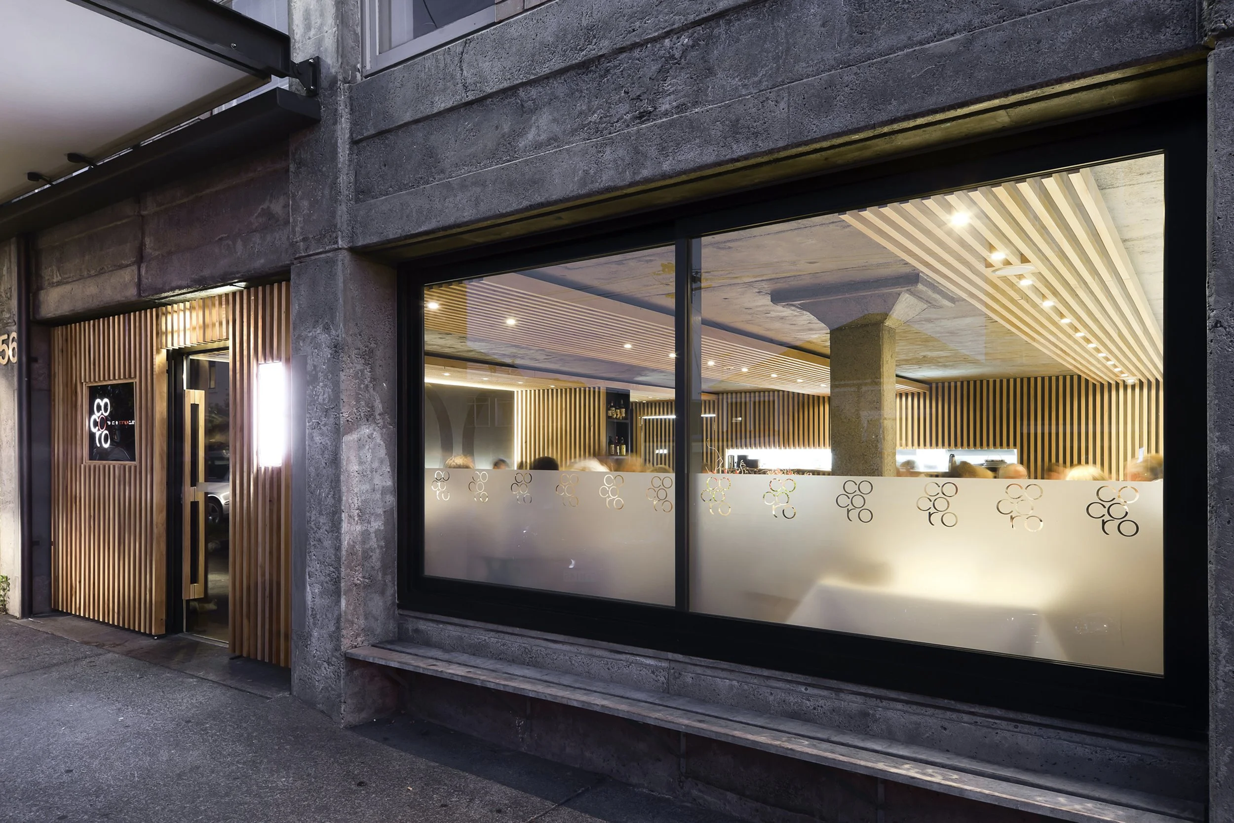 The restaurant from the street at night, the timber ceiling seen through the long window