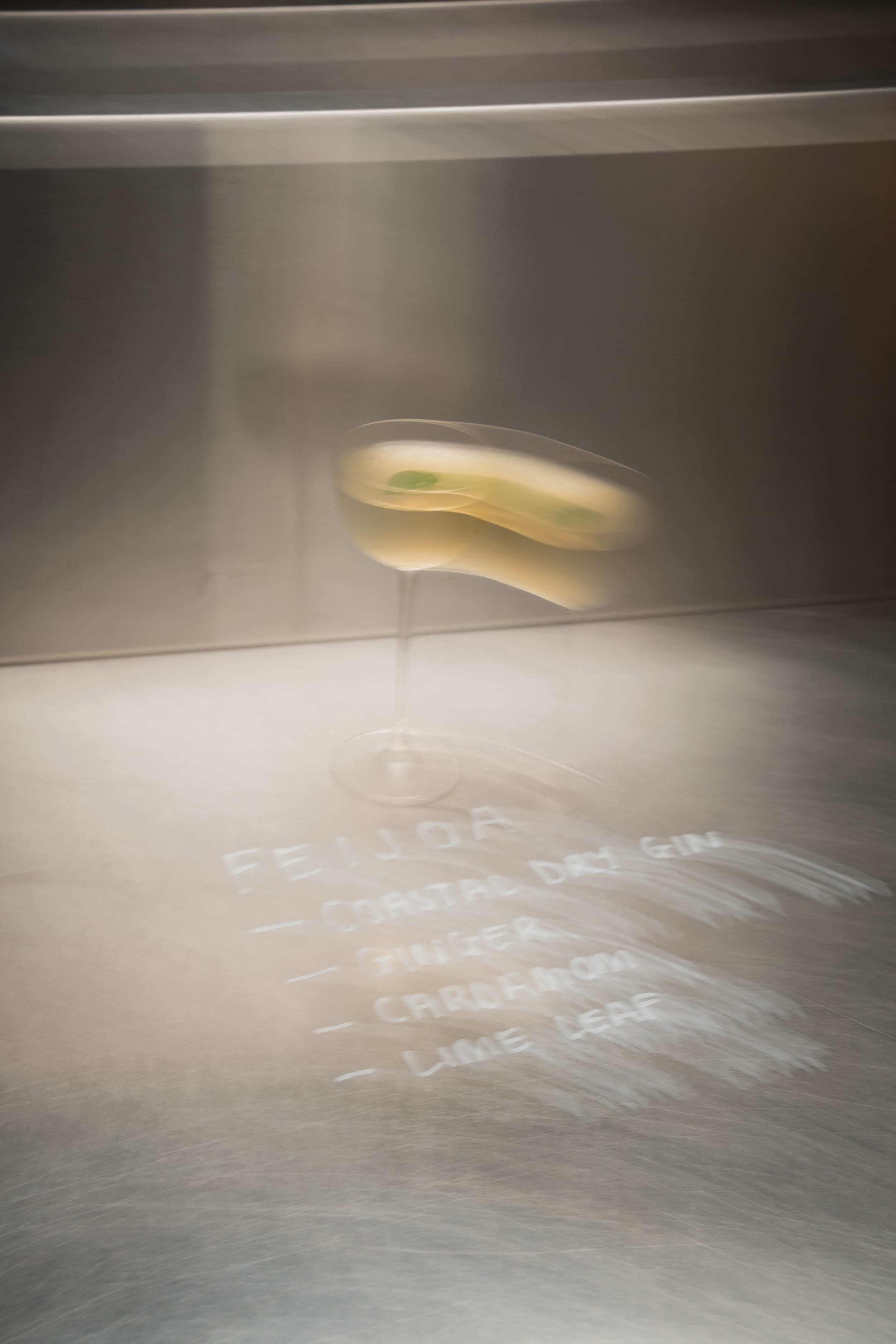 A martini glass with a green olive garnish, illuminated to project shadows with text reflected on a surface below.