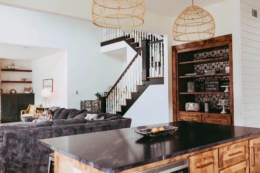 Open-concept living room and kitchen with staircase, wooden shelves, and pendant lights.