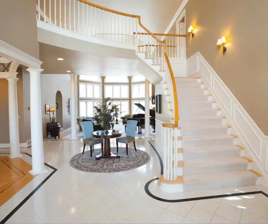 Elegant living room with white staircase, curved balcony, and large windows in the background.