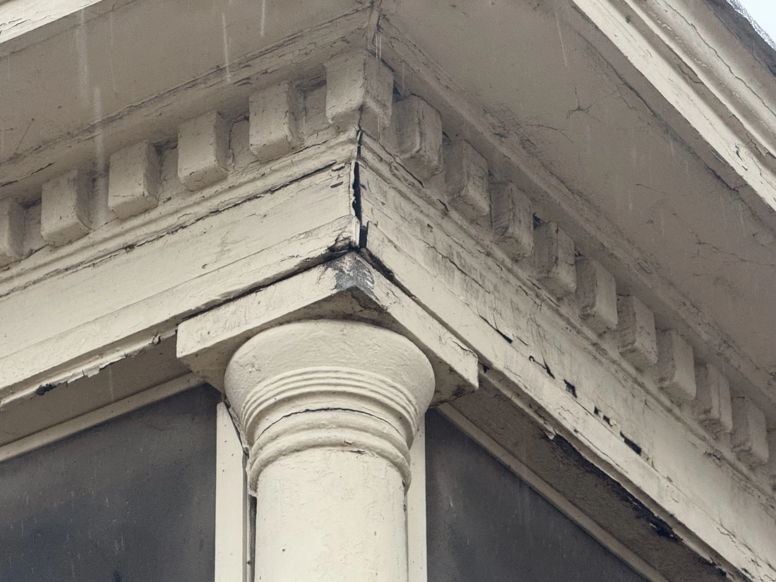 Close-up of an ornate, painted architectural cornice at a building corner with a decorative column below.