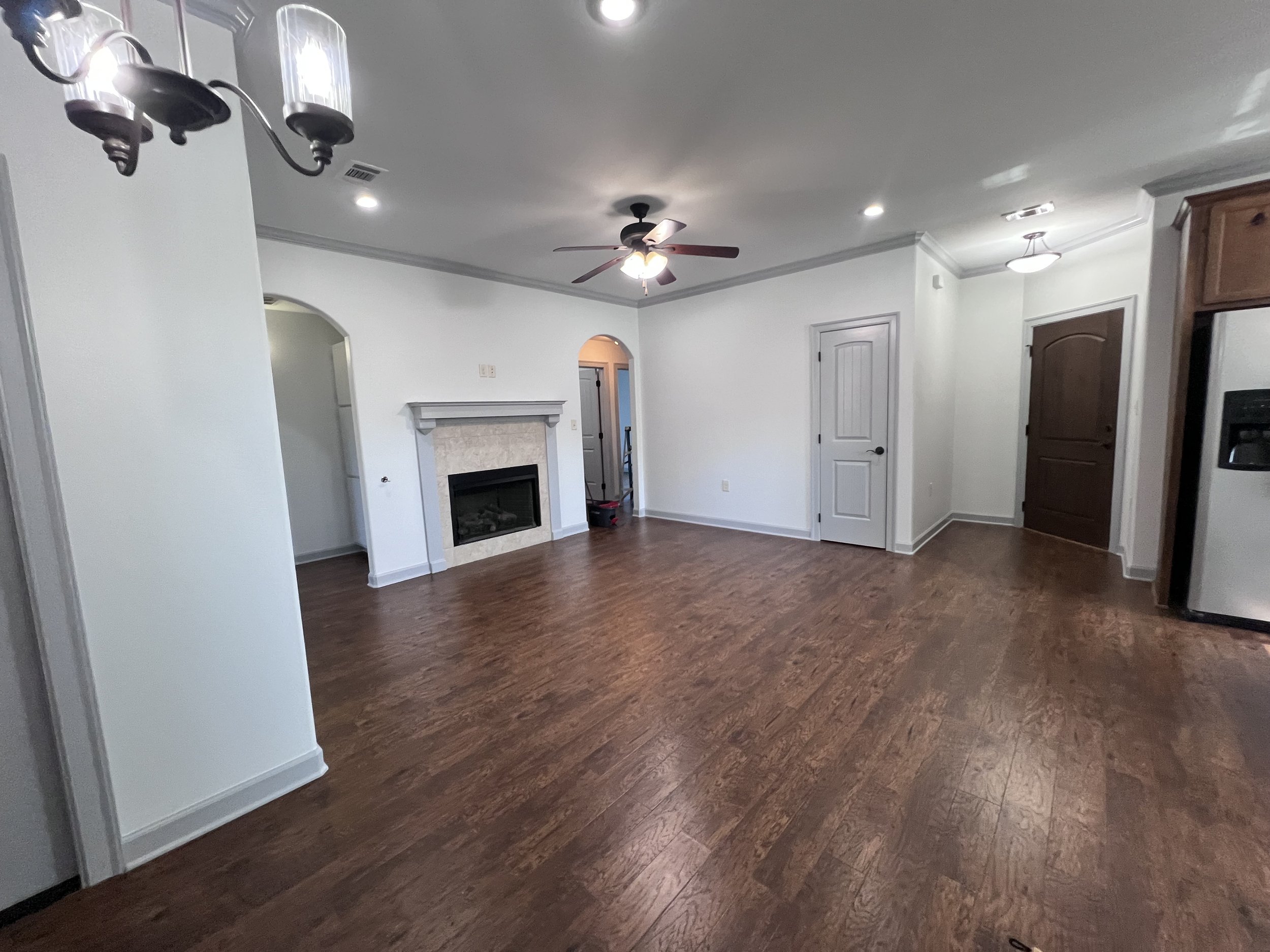 Empty living room with wood flooring, white walls, a fireplace, ceiling fans, built-in cabinets, and recessed lighting.