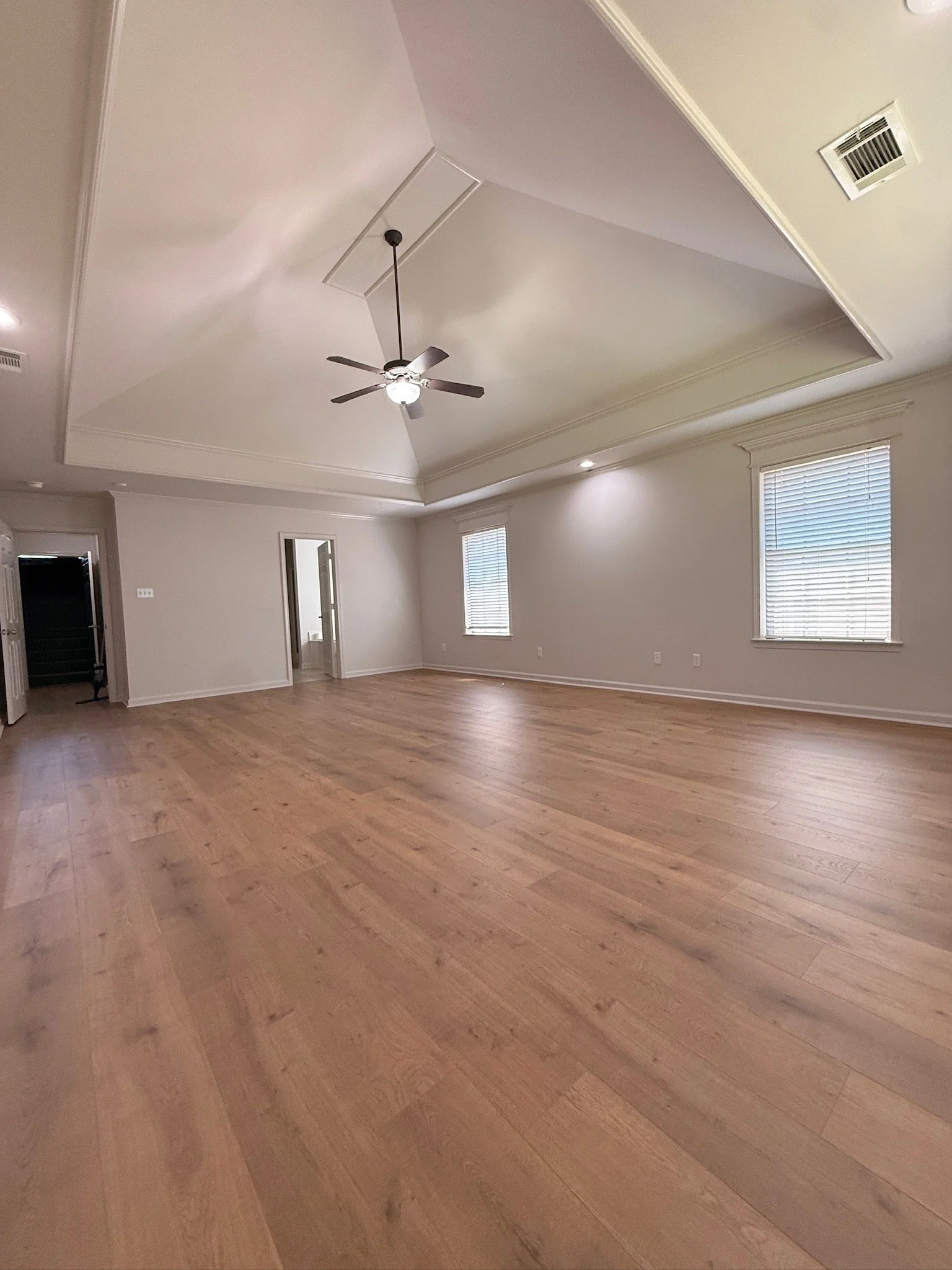 Empty room with light hardwood flooring, white walls, two windows with blinds, a ceiling fan, and recessed lighting.