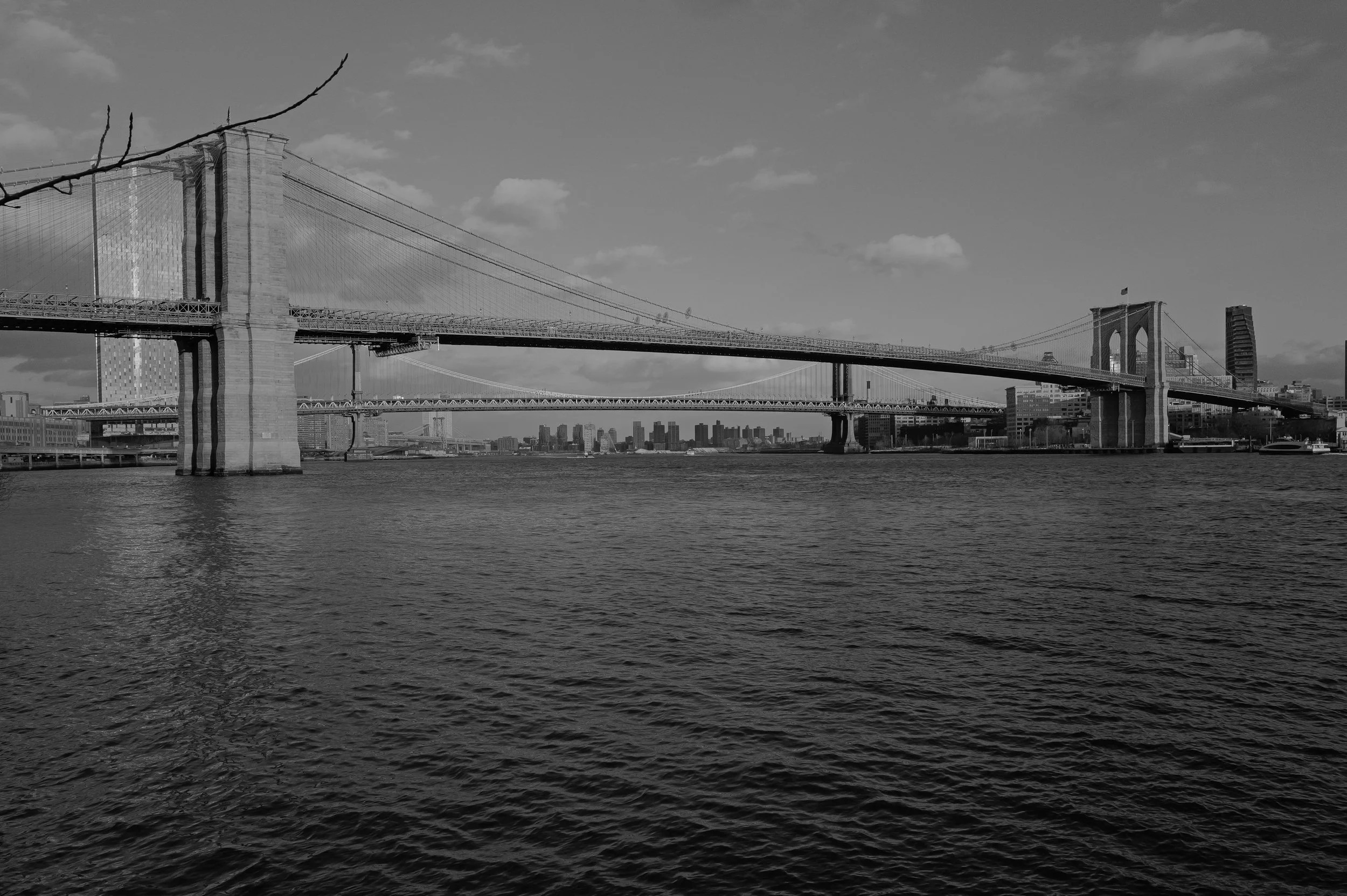 Vue du pont de Brooklyn avec la skyline de New York en arrière-plan, en niveau de gris.