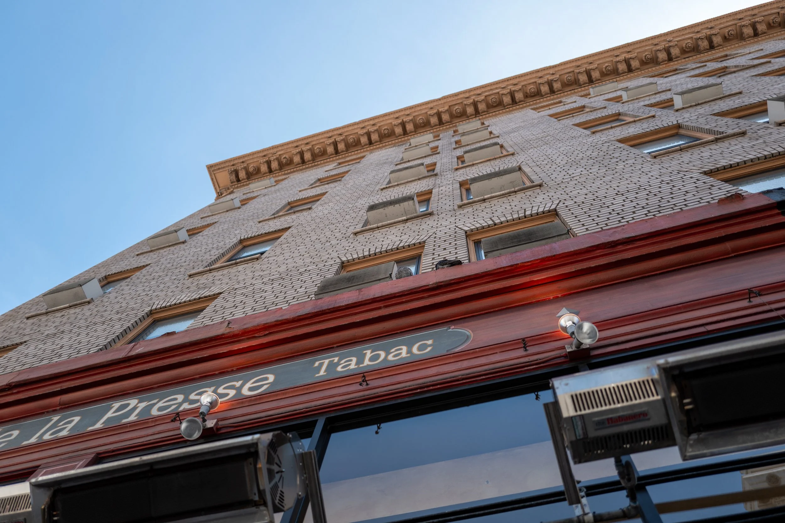 Façade d'un bâtiment résidentiel avec un commerce en bas, au-dessus duquel on peut voir des fenêtres avec des volets fermés. Signage du commerce indiquant 'La Presse Tabac'.