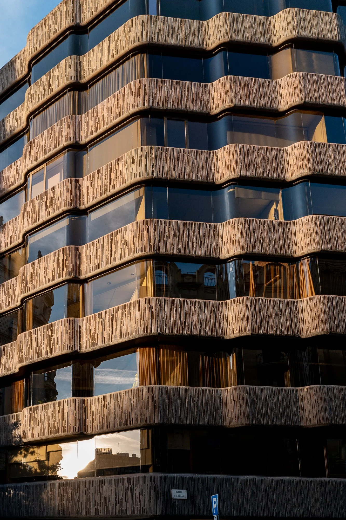 Façade d'un immeuble moderne avec des balcons courbés en béton au crépuscule, reflets du ciel dans les fenêtres en verre.