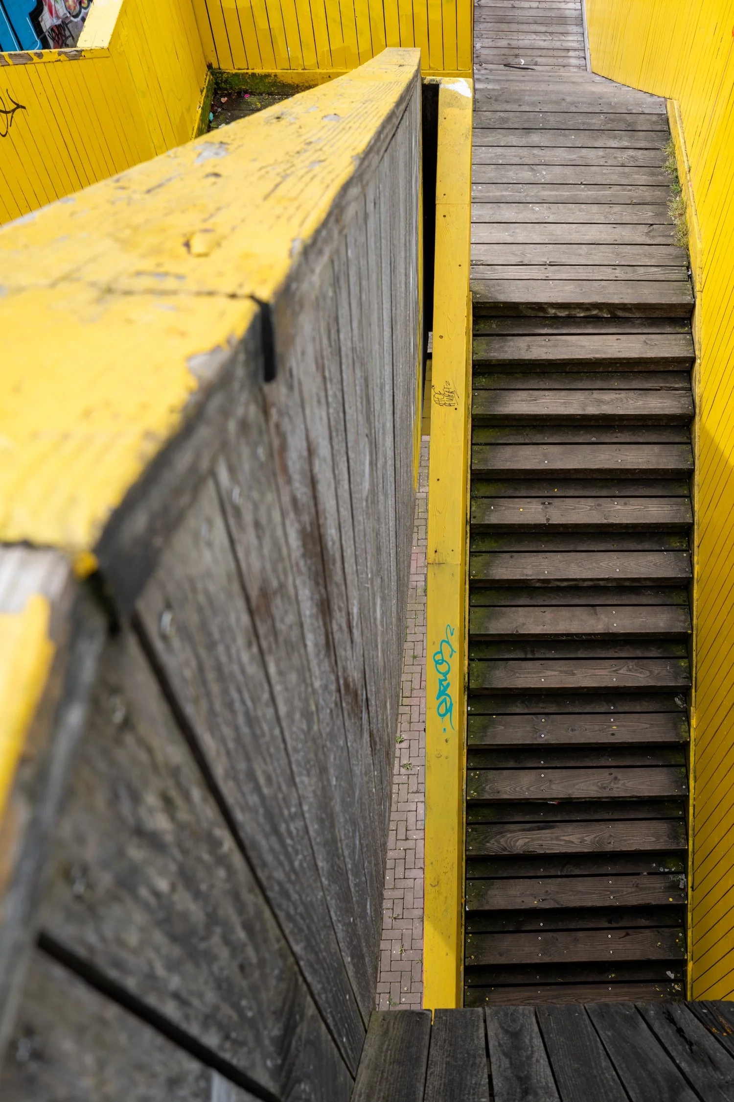 Escalier en bois avec marches sombres et barrières en bois avec peinture jaune autour.