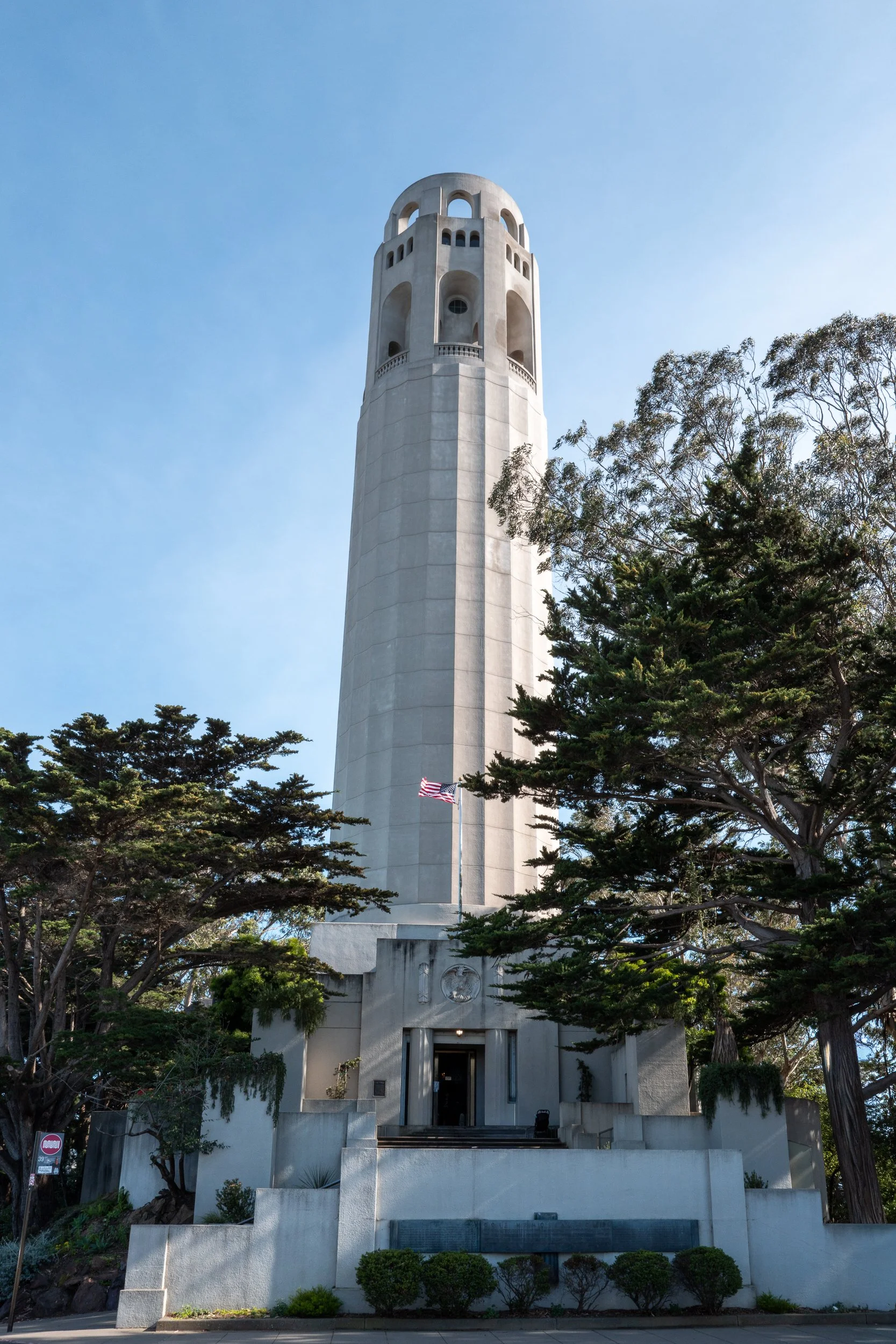 Tour de l'horloge de San Francisco, bâtiment historique en pierre clair avec un drapeau américain devant, entouré d'arbres.