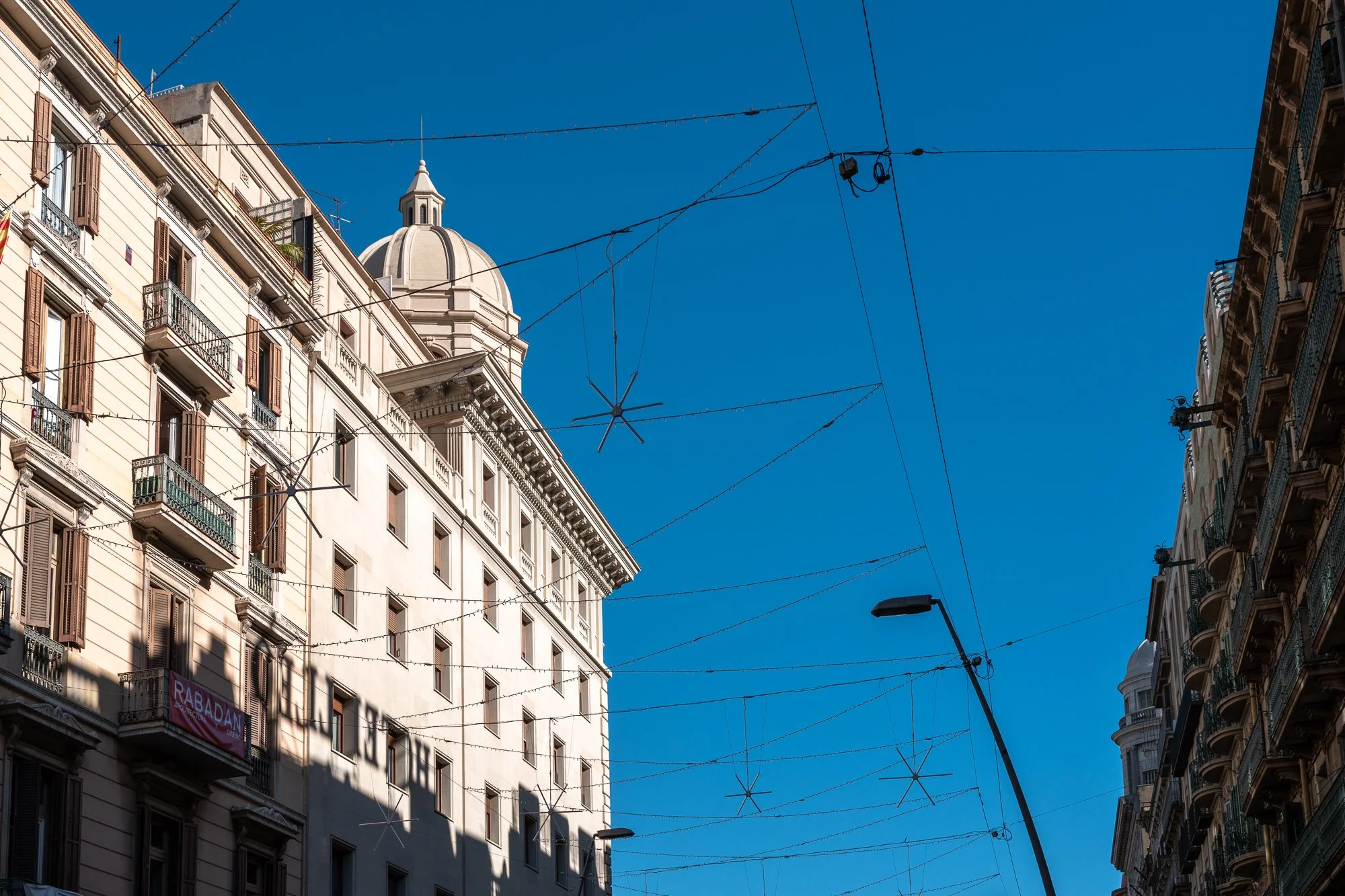 Vues de bâtiments européens avec des fenêtres et des balcons, des câbles électriques suspendus en travers de la rue et un ciel bleu clair.