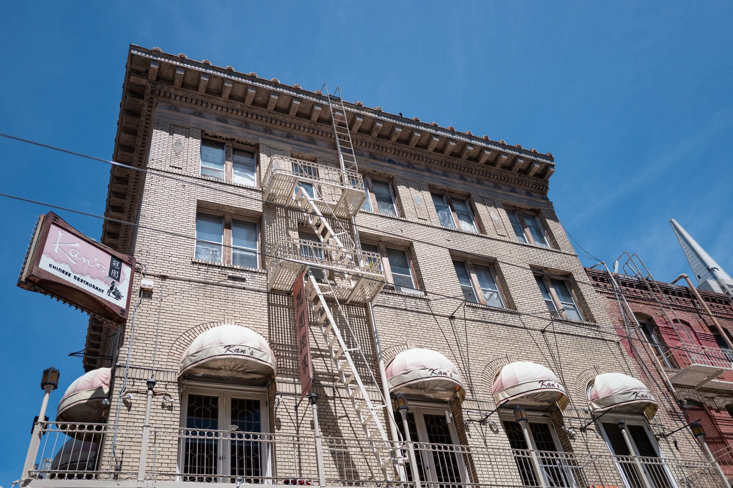 Facade d'un immeuble en briques avec des fenêtres, des balcons en fer forgé, un tourne-disque Installé pour un nettoyage ou une réparation, et un signe de restaurant chinois nommé 'Kani'.