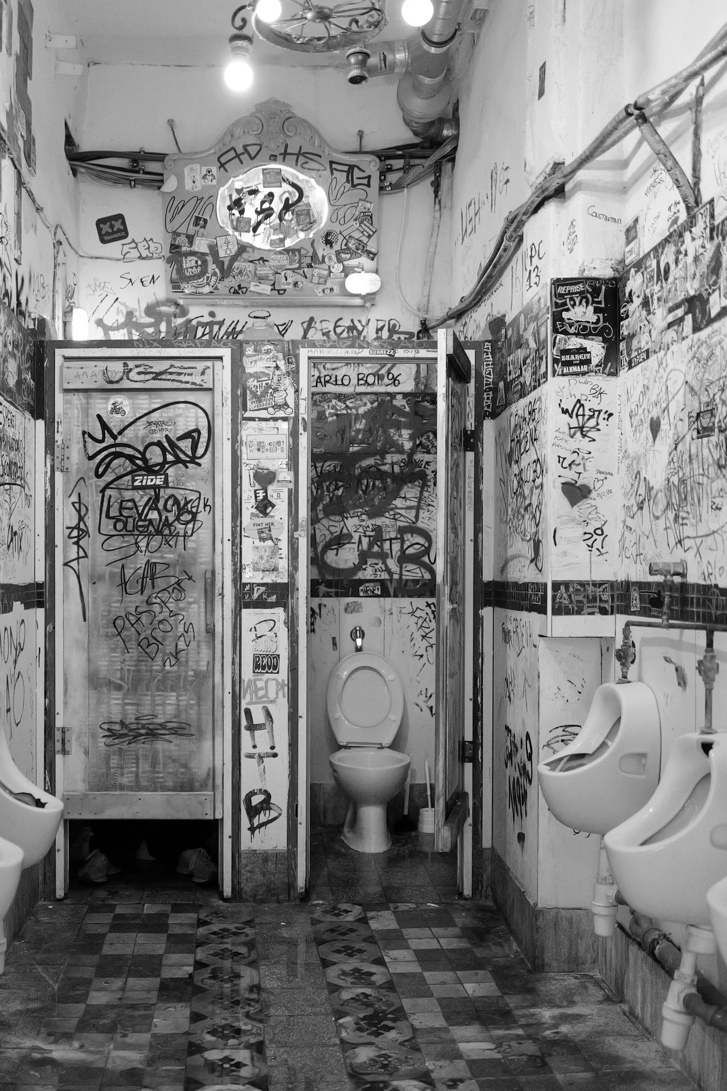 Une cabine de toilettes publiques sale et recouverte de graffitis, avec deux toilettes et un mur en arrière-plan