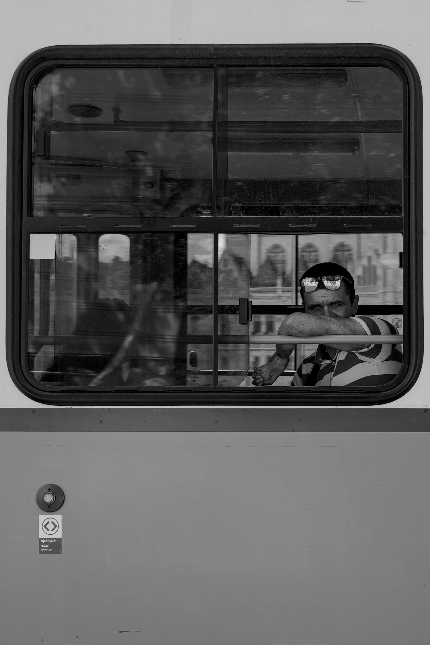 Homme portant des lunettes de soleil, assis dans une cabine de bus, regardant à travers la fenêtre.