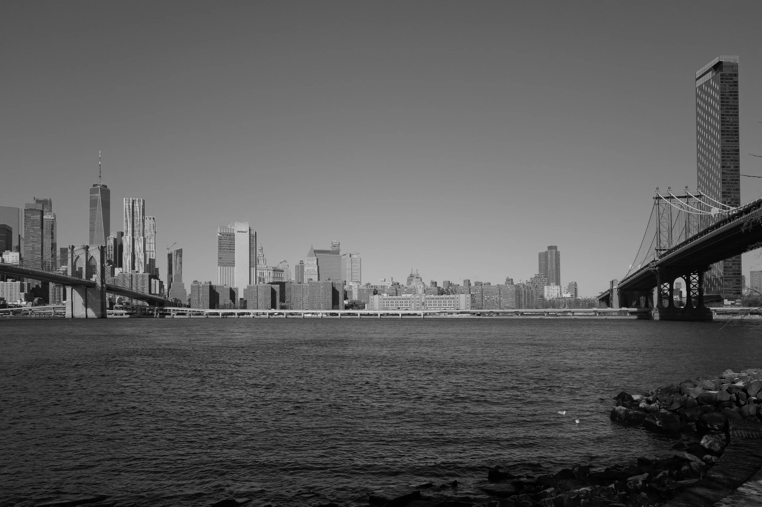 Paysage urbain de Manhattan avec la skyline de New York, ponts et fleuve en premier plan, en version noir et blanc.