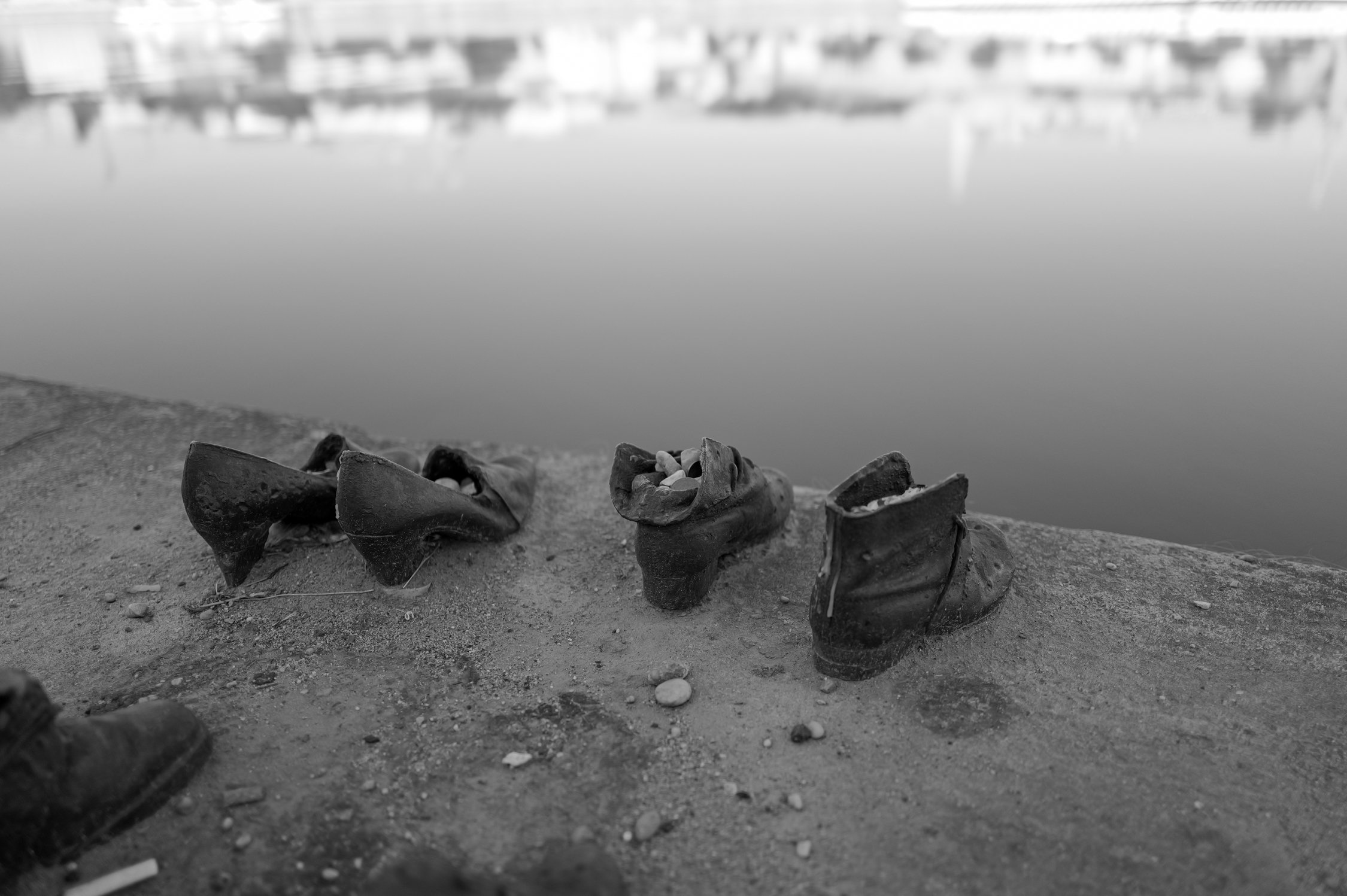 Restes de chaussures en cuir abandonnées sur une plage de sable, avec des bâtiments et un port en arrière-plan.