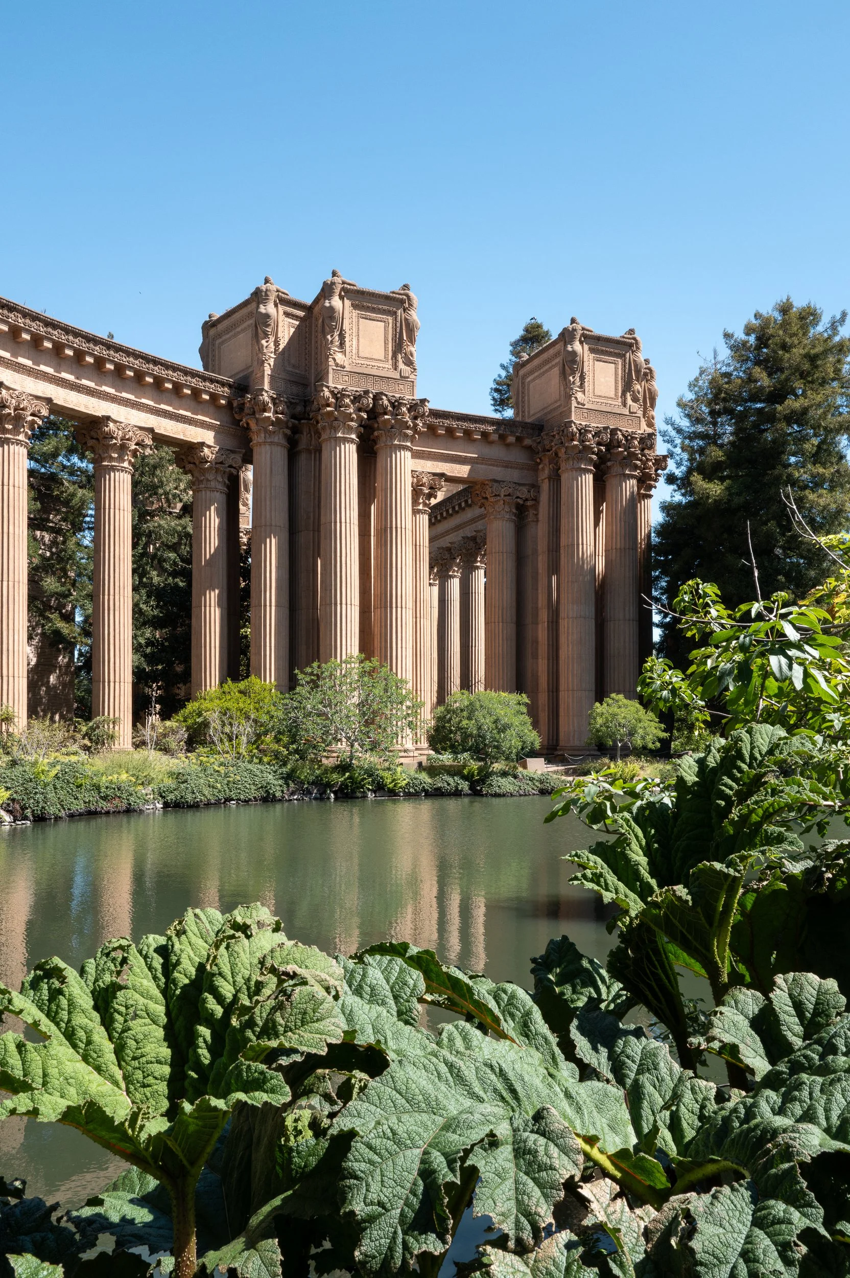 Ruines antiques avec colonnes et fontaine entourée de végétation.
