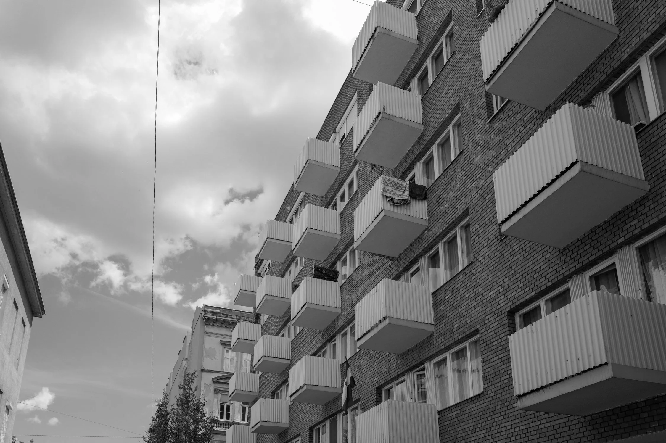 Bâtiment résidentiel avec plusieurs balcons en saillie en face, et des fenêtres. Le ciel est nuageux.