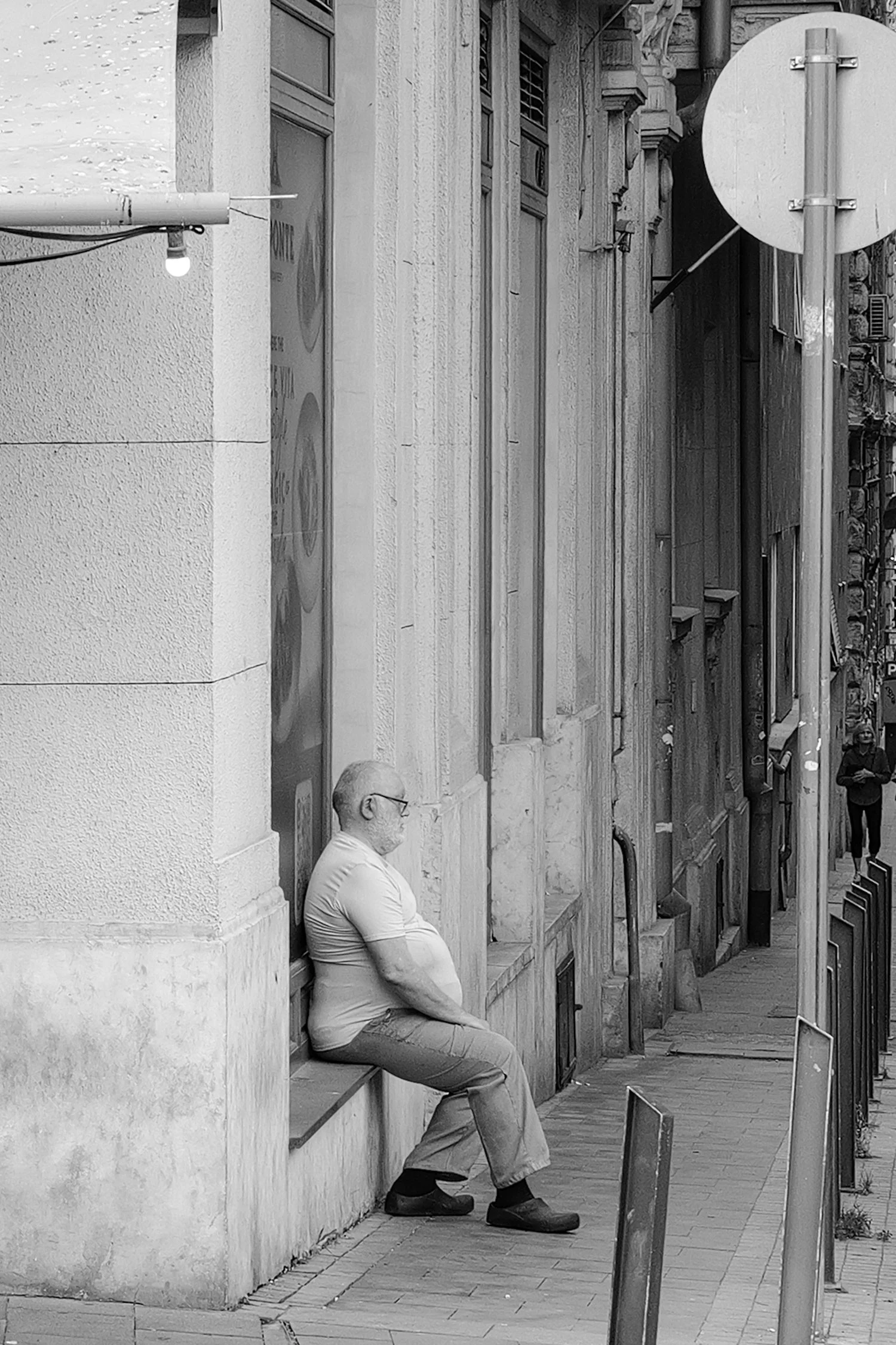 Un homme assis et un autre qui se tient debout sur un trottoir, dans une rue urbaine, avec des bâtiments en arrière-plan.