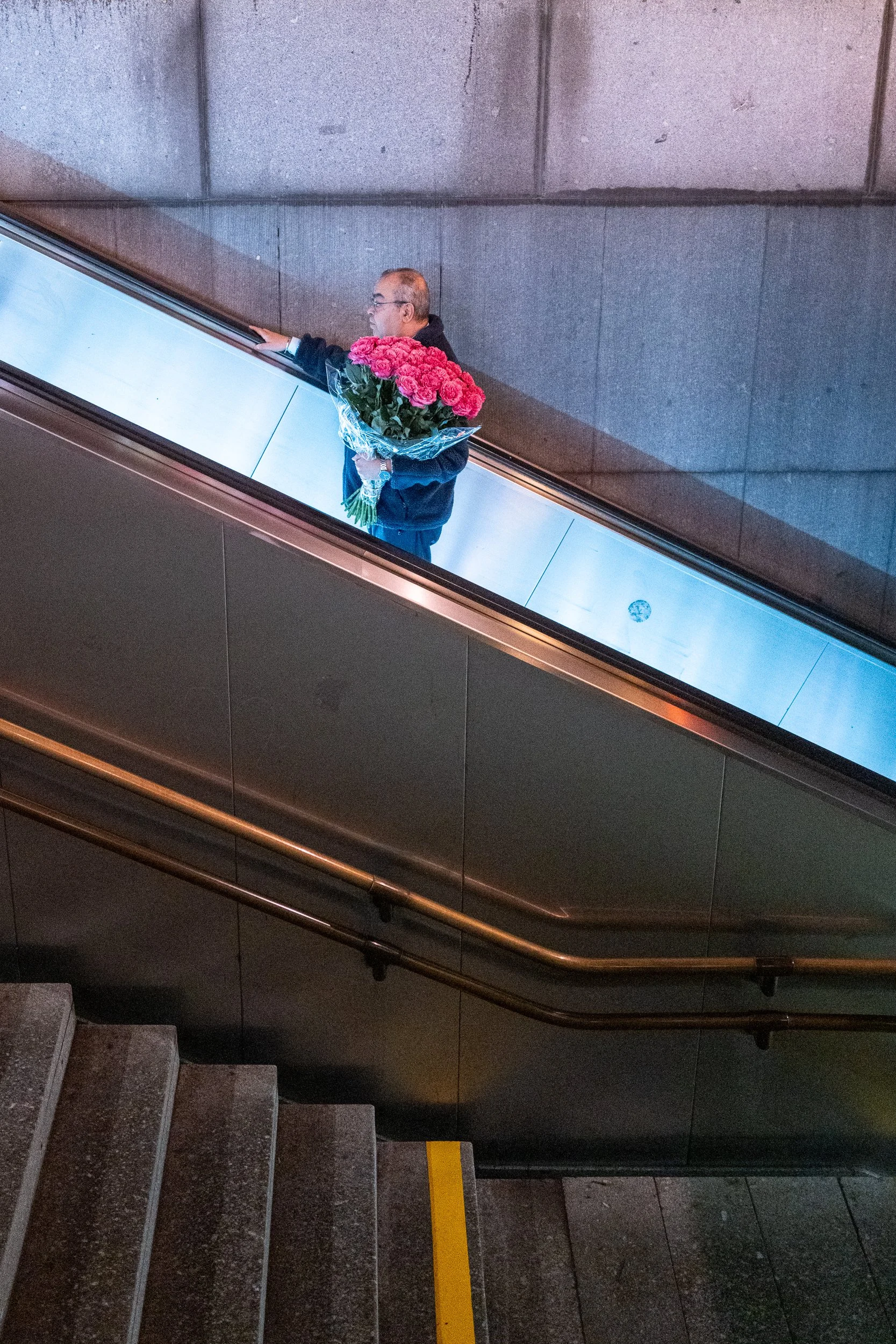 Un homme tenant un bouquet de roses roses monte un escalier en milieu urbain.