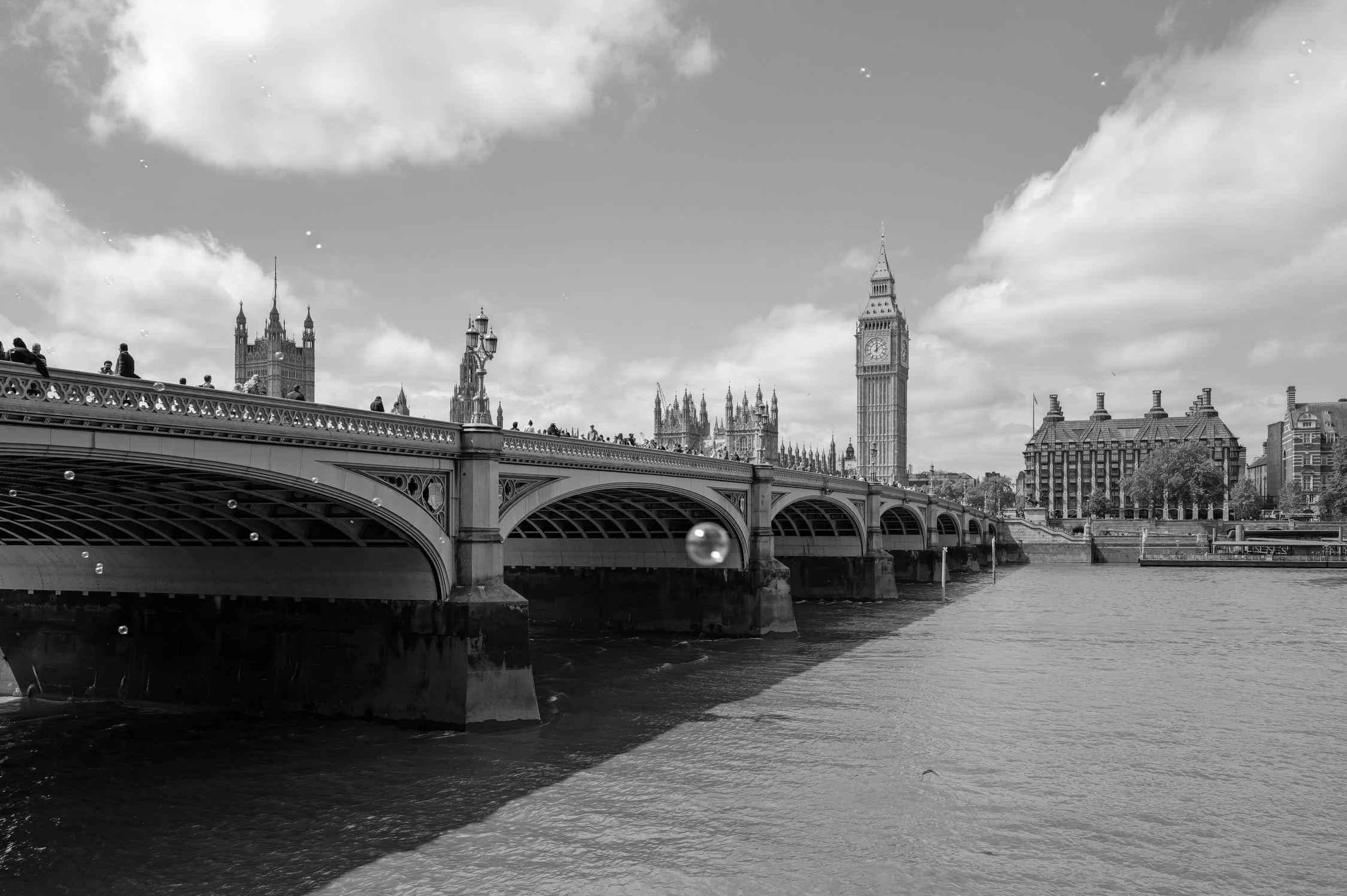 Vue en noir et blanc du pont de Westminster et du Big Ben à Londres, avec des touristes sur le pont et la rivière en dessous.