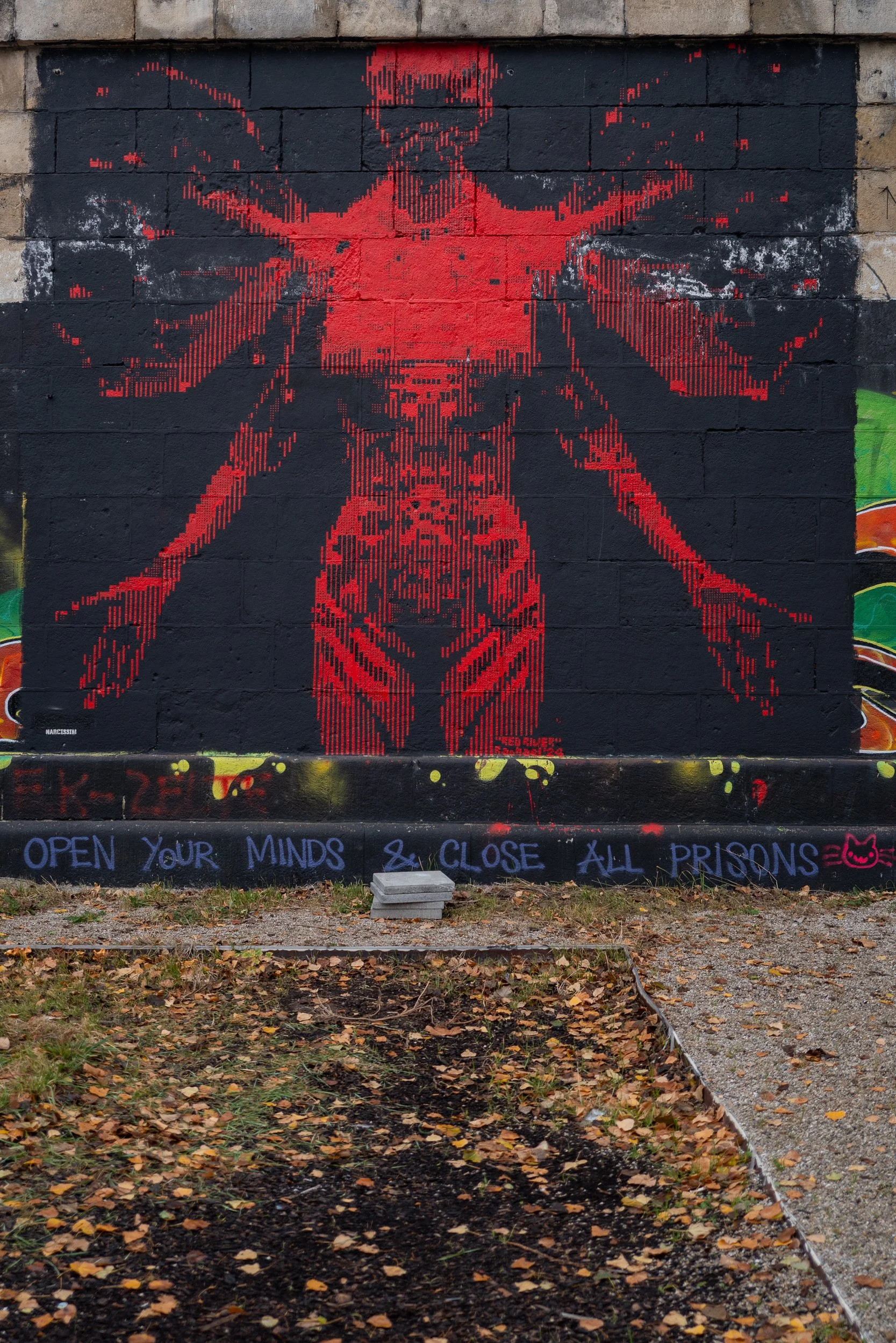 Pochoir de la figure de la Vierge Marie en rouge sur un mur noir avec un message en bas disant "Ouvre ton esprit et ferme toutes les prisons"