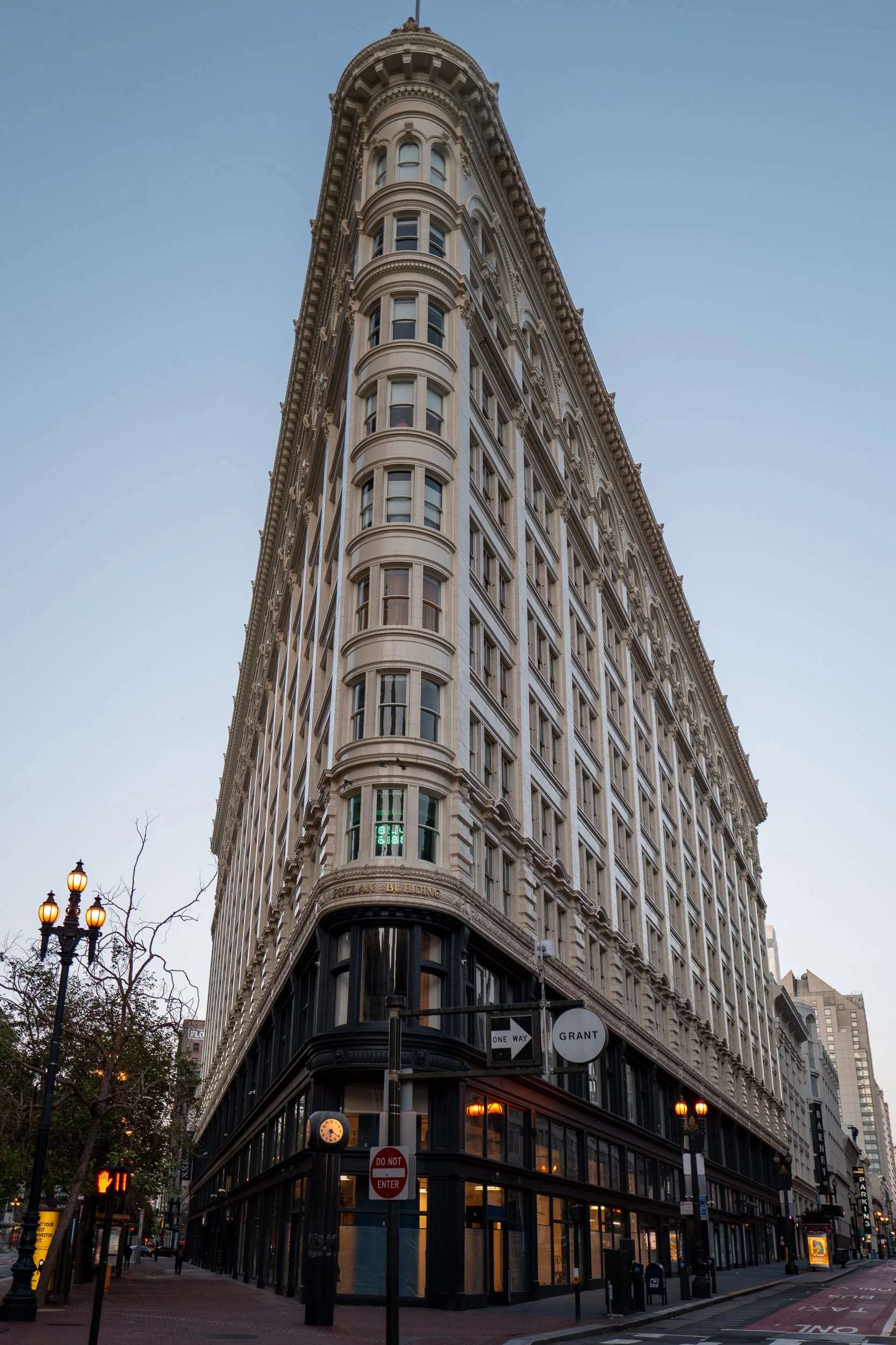 Bâtiment ancien avec architecture détaillée, grande façade en pierre blanche, coin de rue urbain avec lampadaires et panneaux de signalisation, ciel clair.
