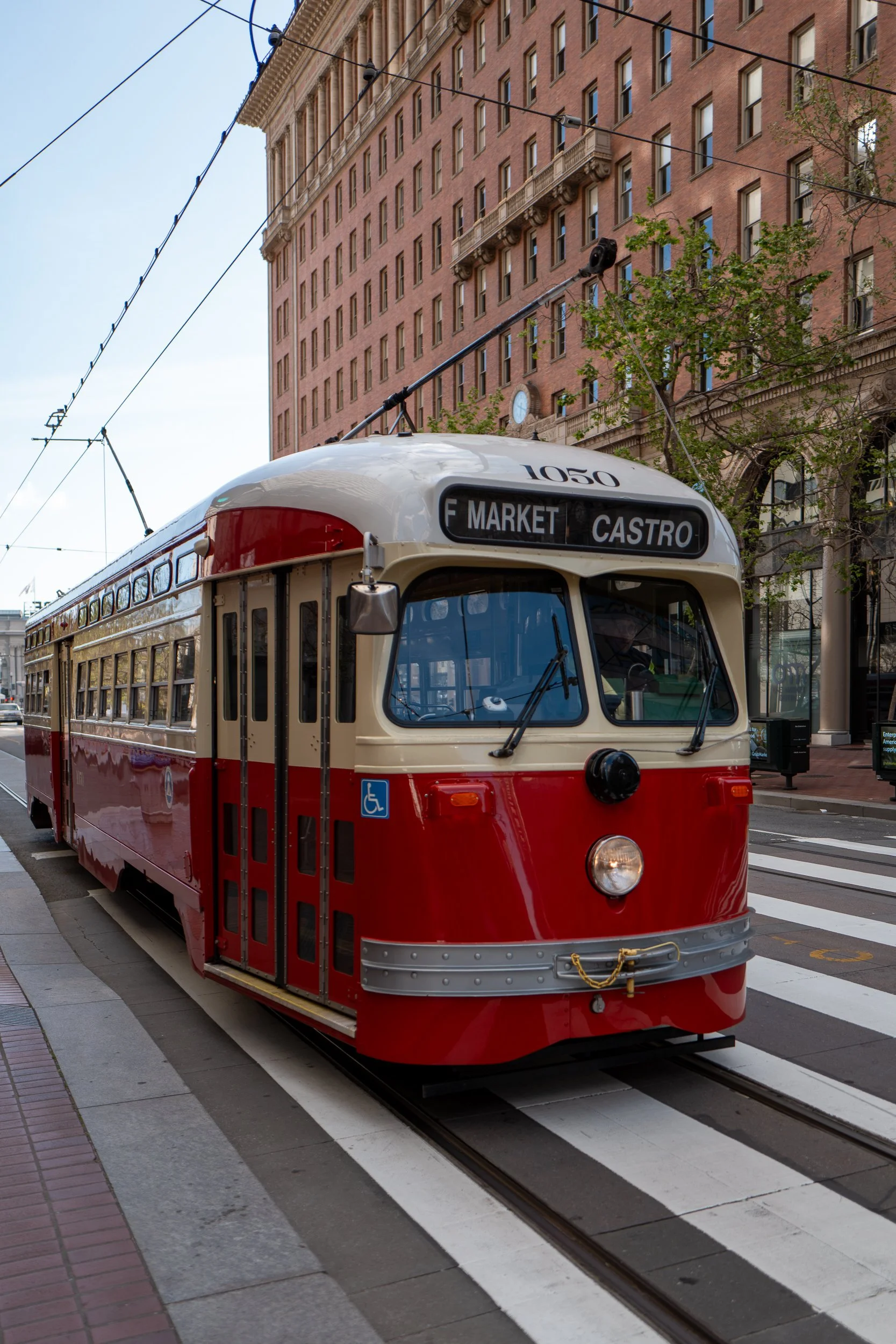 Un tram rouge et blanc en mouvement sur une voie urbaine avec un bâtiment en fond.
