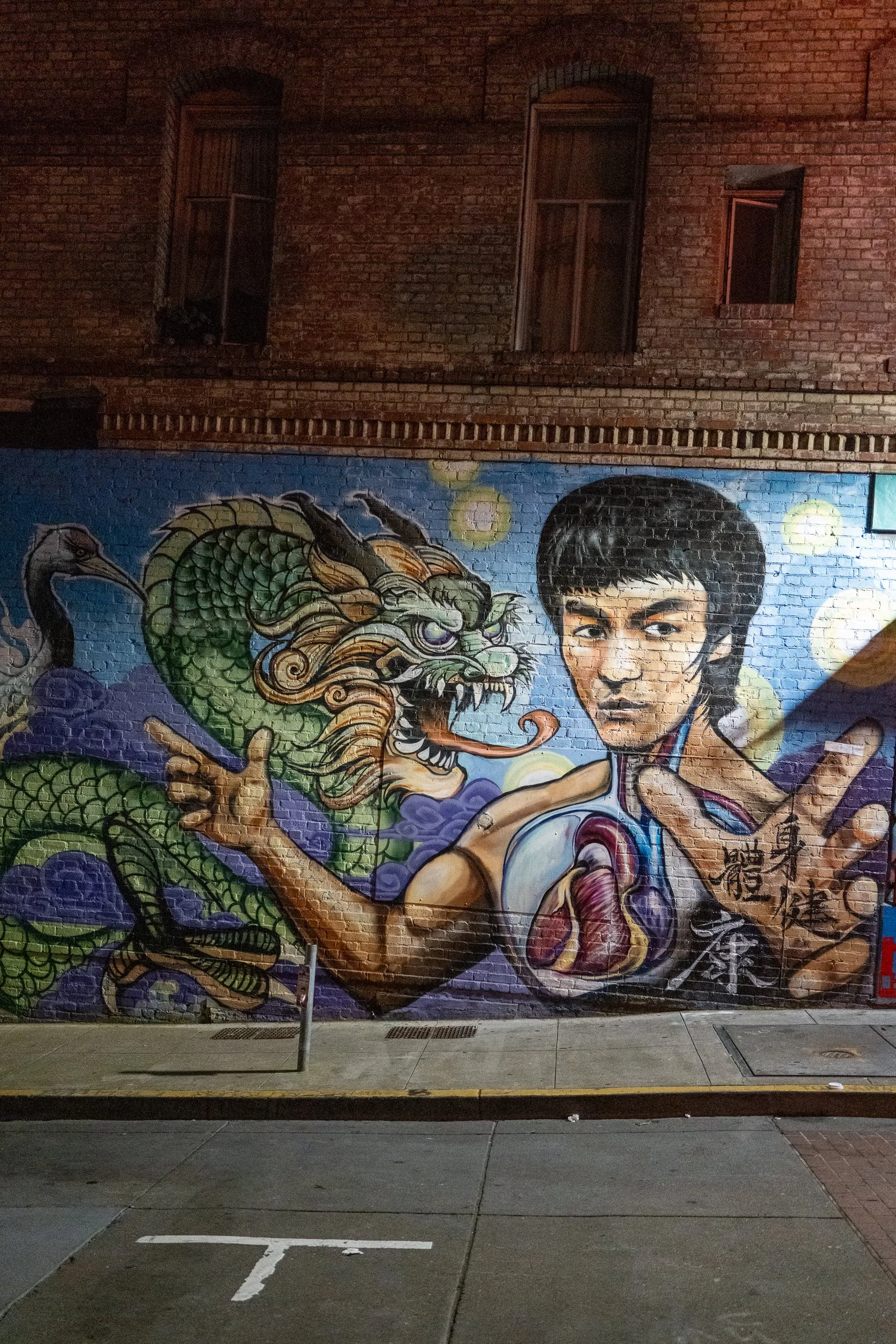 Graffiti représentant un dragon et un jeune homme chinois faisant un geste martial sur un mur en briques.