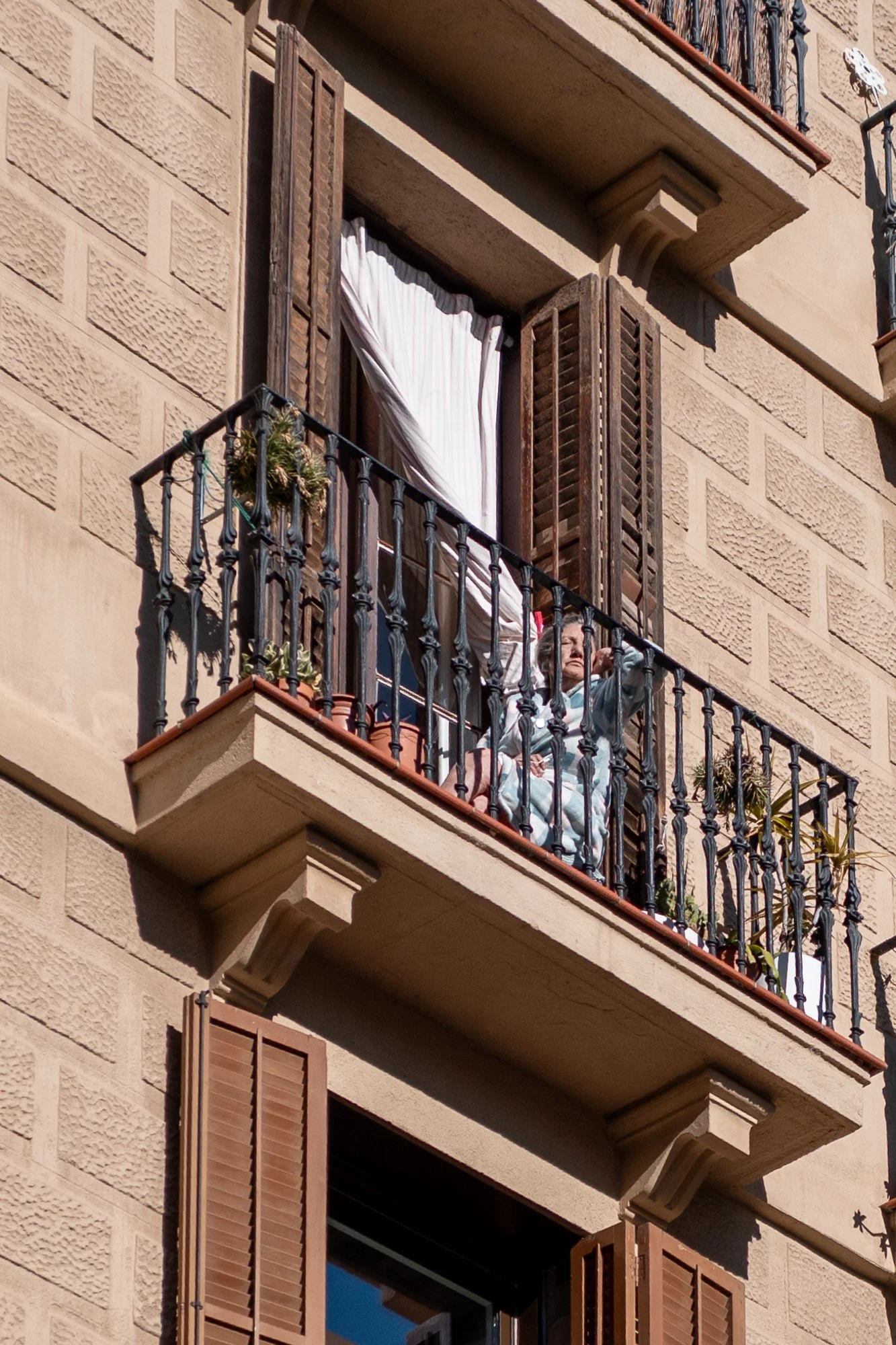 Balcon avec des volets en bois, une femme âgée parle au téléphone.