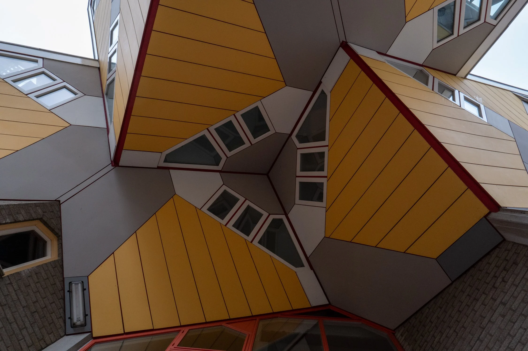 Vue en contre-plongée d'un bâtiment moderne avec façade colorée en jaune, gris et rouge, caractérisé par des formes géométriques et des fenêtres en forme d'hexagone.