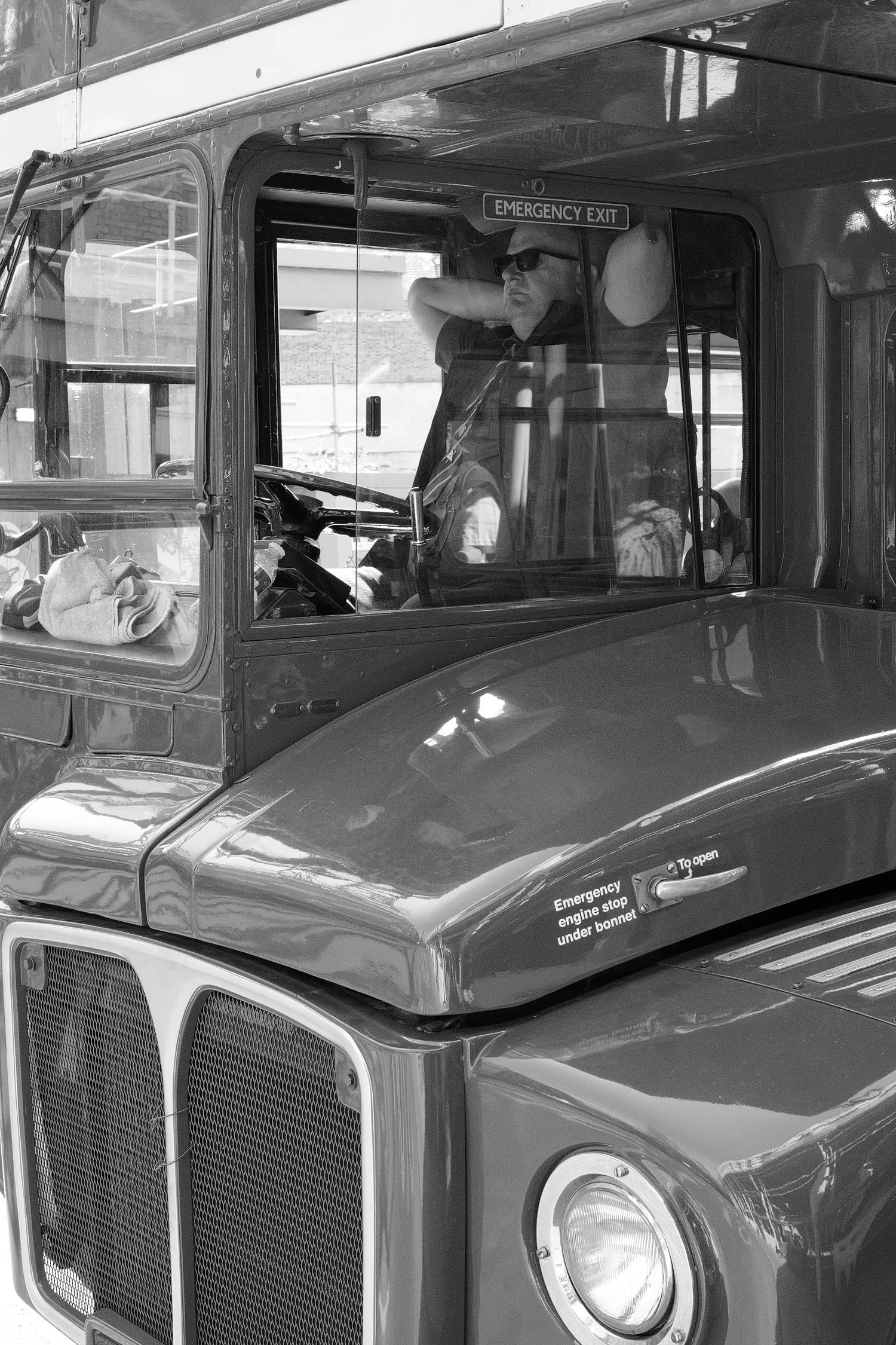 Un camion gris avec un homme portant des lunettes de soleil à l'intérieur du véhicule, regardant par la fenêtre, avec une plaque indiquant la sortie de secours d'urgence.