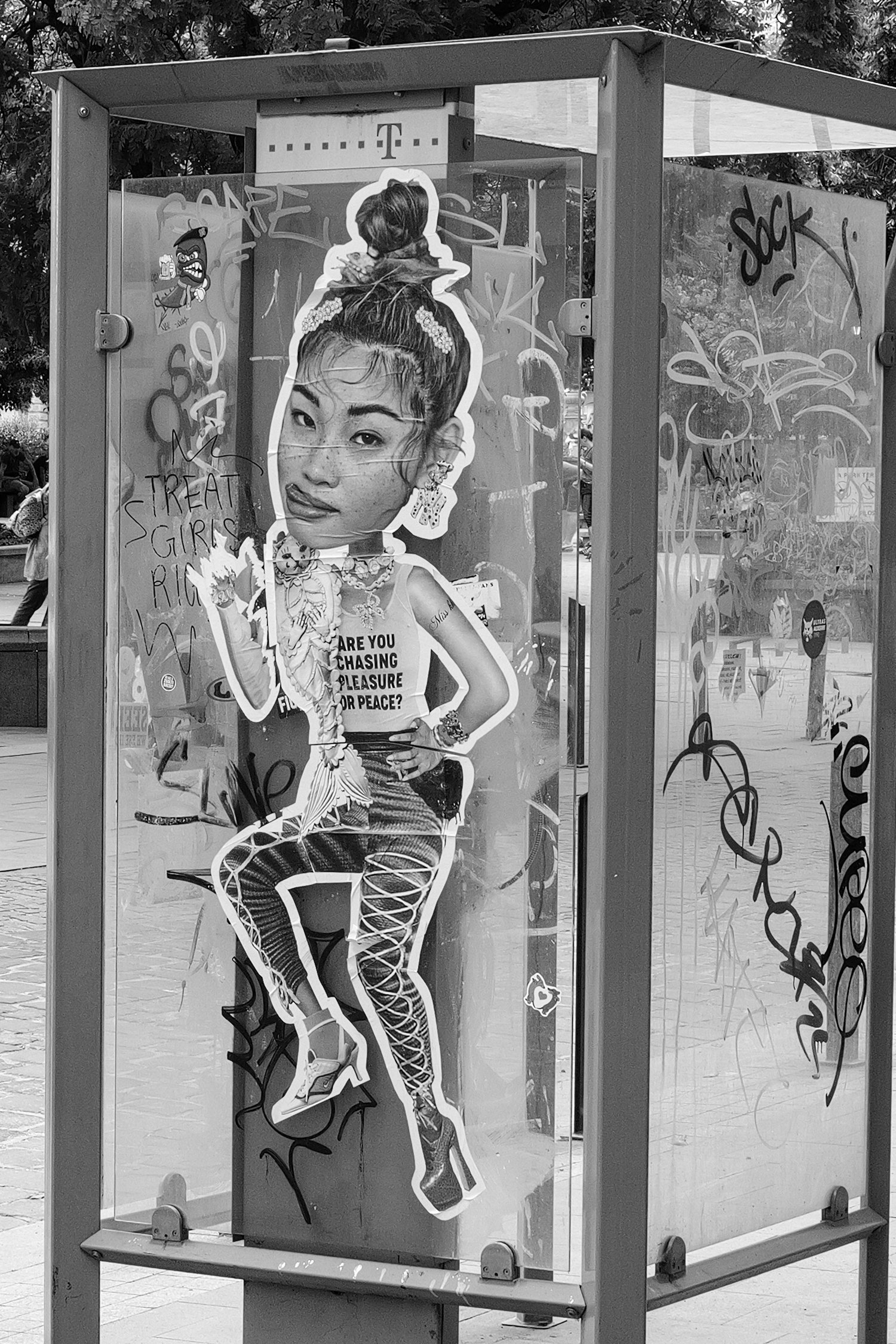Illustration d'une jeune femme avec des cheveux en chignon体验ous, portant des vêtements à motifs, tenant une canette dans une main, posé dans une cabine téléphonique recouverte de graffiti dans un environnement urbain.