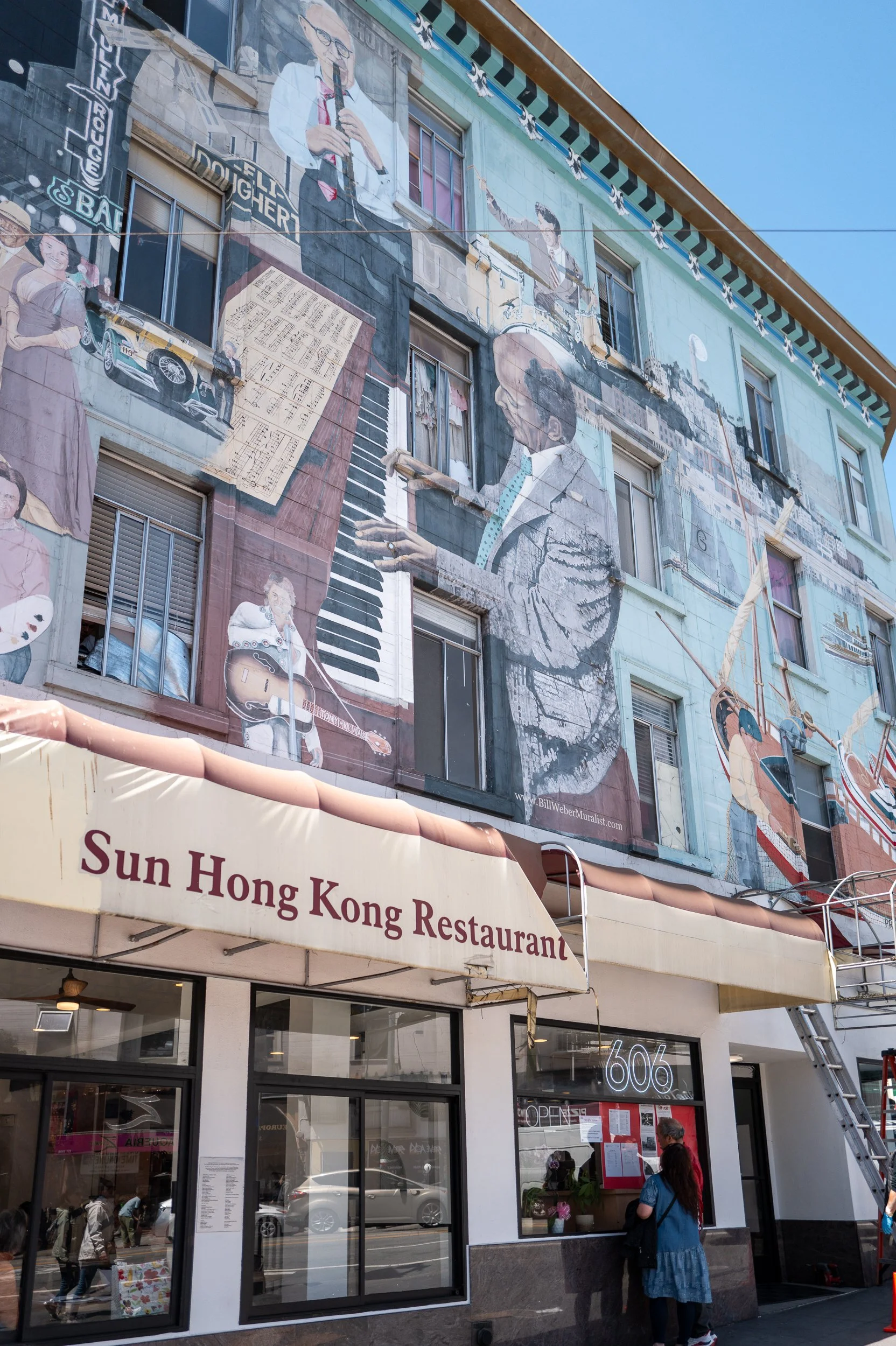 Une fresque murale représentant des musiciens, un chanteur, un pianiste, un guitariste et un artiste jouant du violon, devant un restaurant chinois nommé 'Sun Hong Kong Restaurant'.