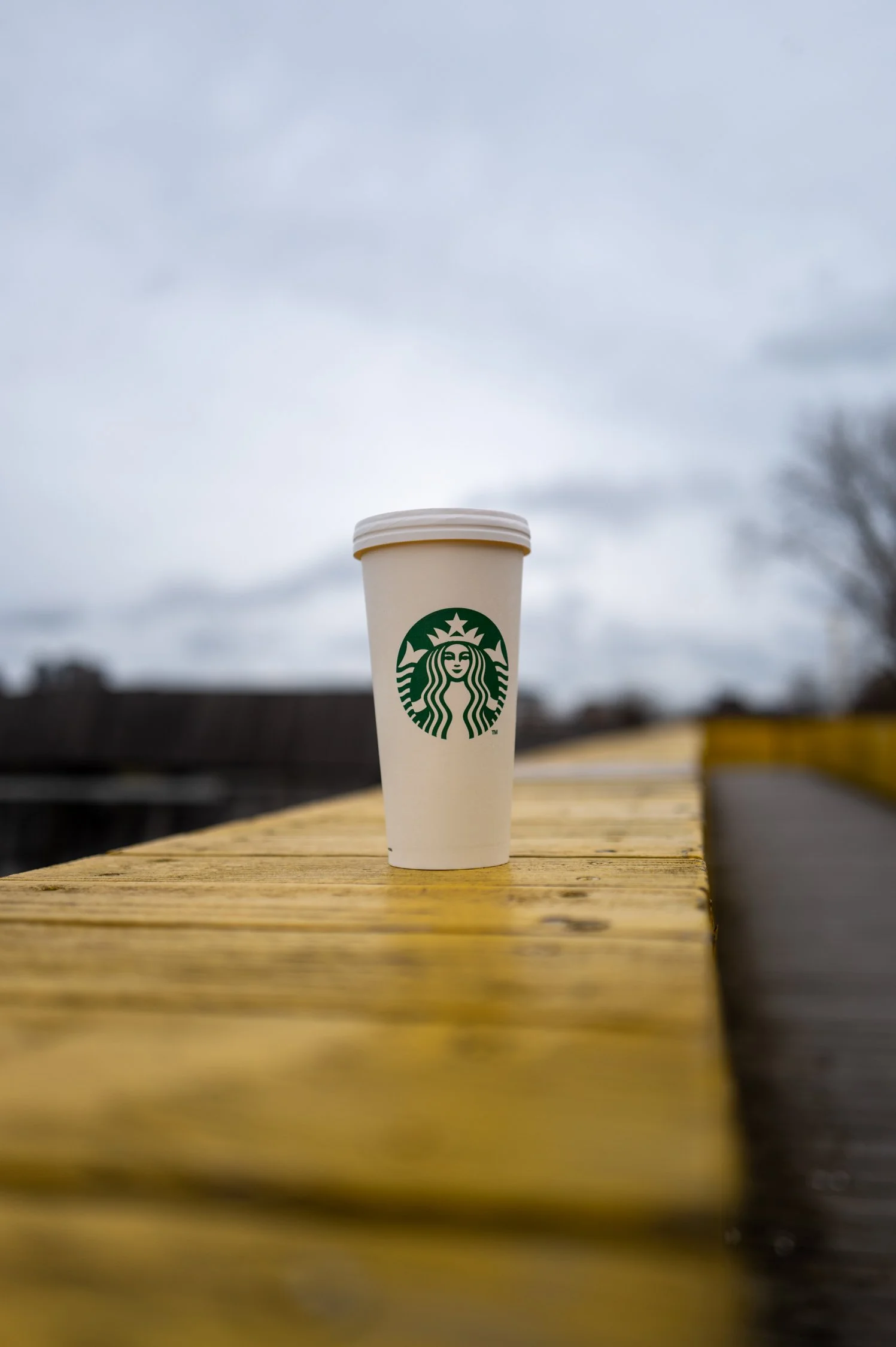 Une tasse à café Starbucks blanche placée sur une table en bois lors d'une journée nuageuse