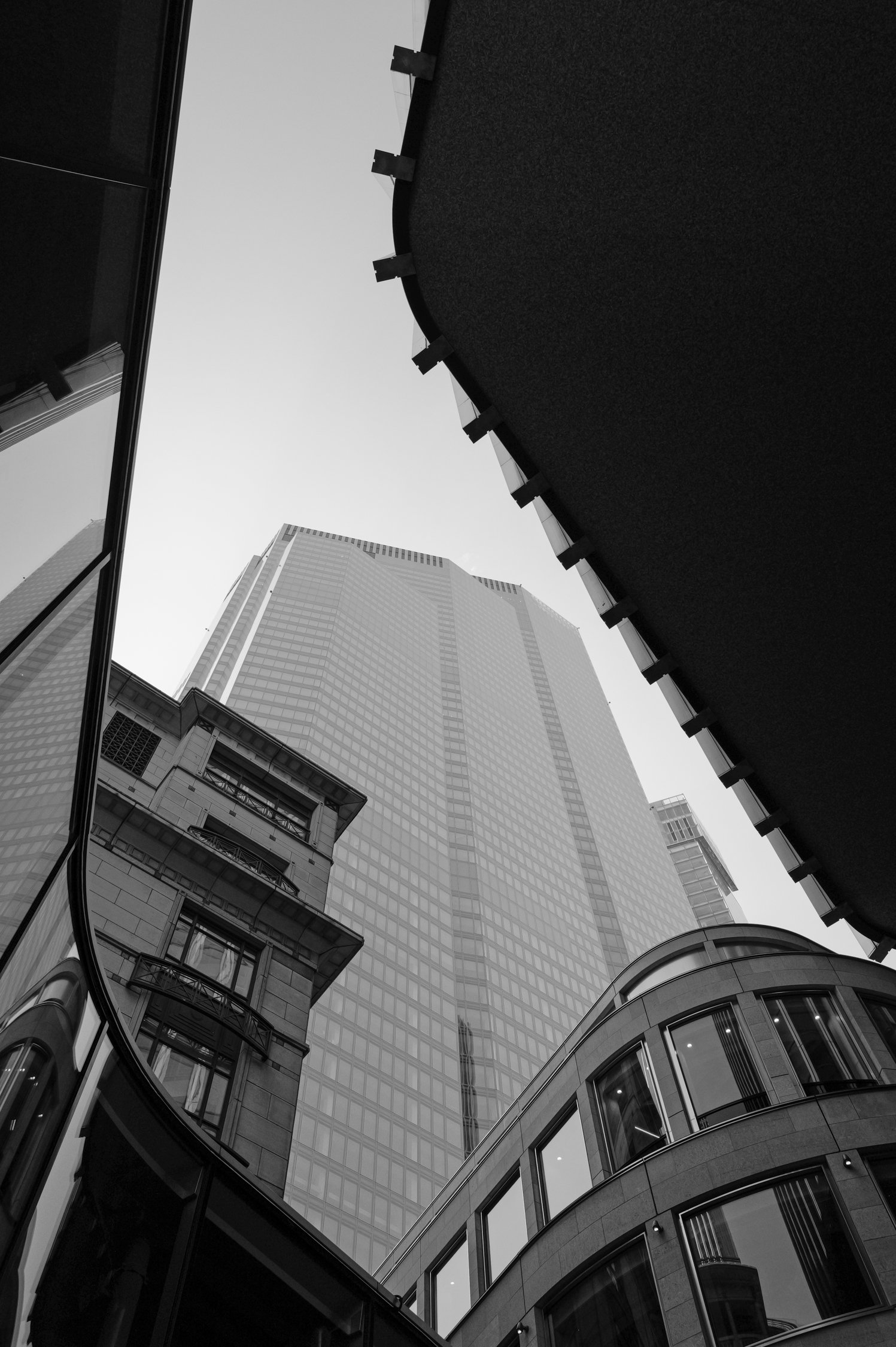 Photo en hauteur montrant des gratte-ciel modernes en verre, reflections de bâtiments adjacents, et un ciel clair dans une zone urbaine.