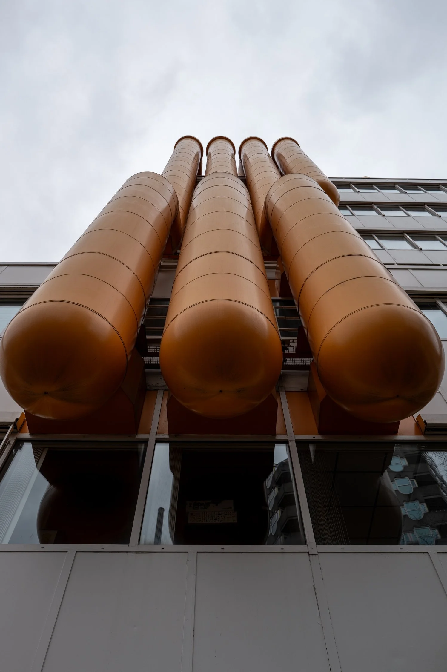 Vue en contre-plongée d'un bâtiment moderne avec quatre grandes cheminée en acier coulé de couleur orange, et une façade en verre et en métal.