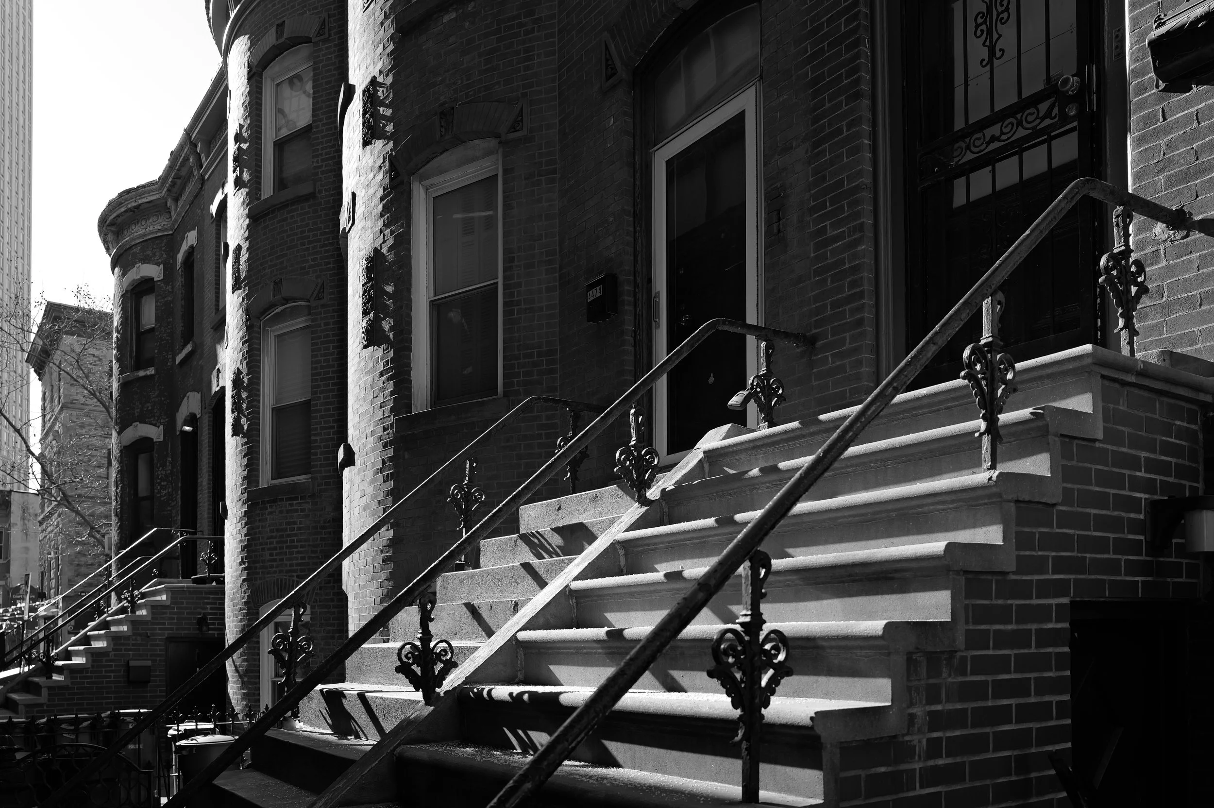 Escalier en pierre menant à une porte d'entrée d'une maison en briques avec des fenêtres en haut, dans un quartier résidentiel.