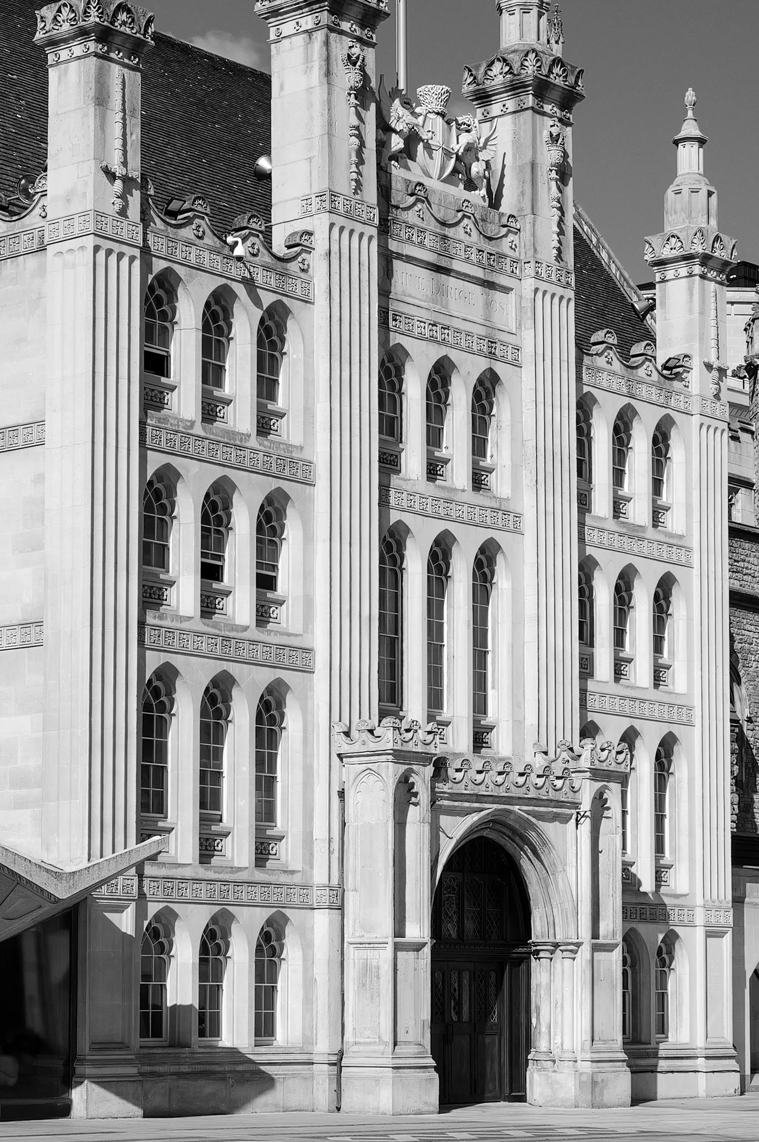 Une façade d'un bâtiment historique avec des fenêtres gothiques, des colonnes et des sculptures détaillées, vue en noir et blanc.