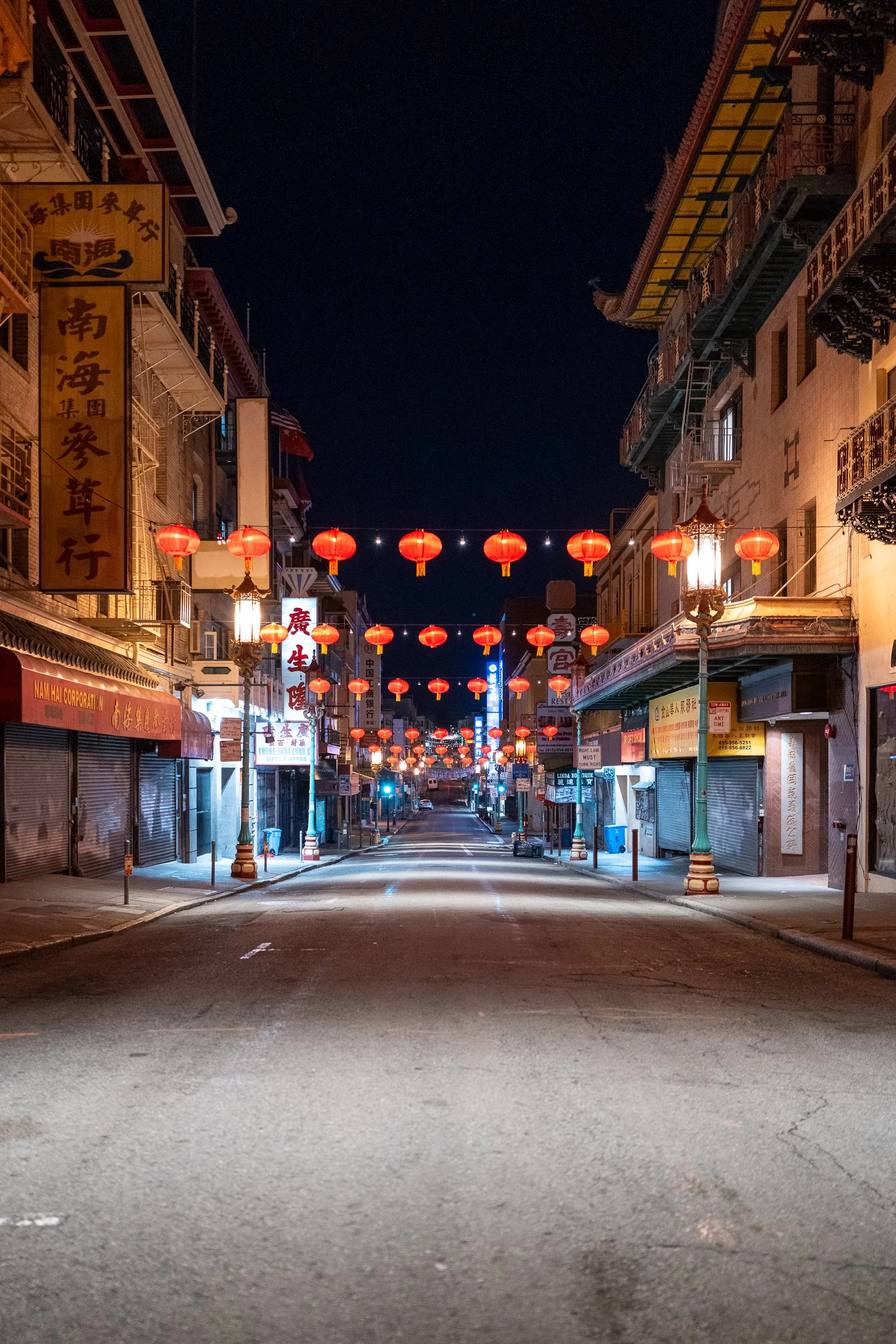 Rue urbaine vide à Chinatown avec des lanternes rouges suspendues au-dessus, bâtiments avec enseignes en chinois, nuit, ambiance calme.