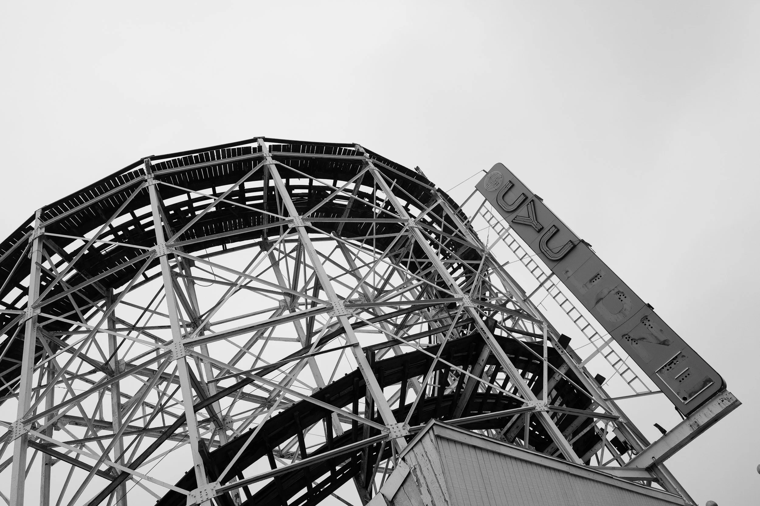Vue en contre-plongée d'une grande roue de fête foraine en structure métallique, avec un panneau lumineux indiquant 'LUXUL' en anglais, dans un ciel nuageux.