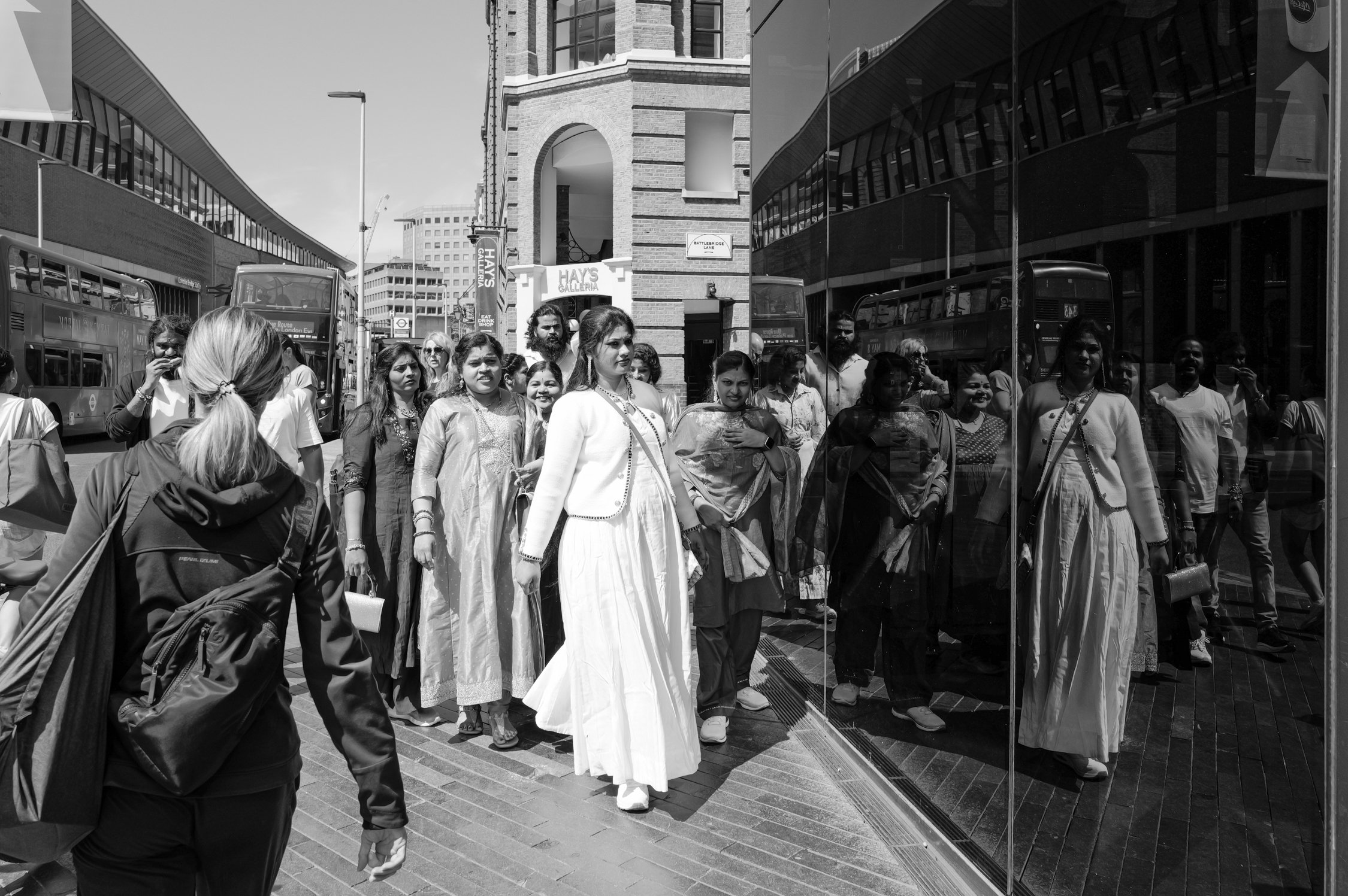 Groupe de personnes portant des vêtements traditionnels indien devant un bâtiment en ville, avec des bus rouges à proximité.
