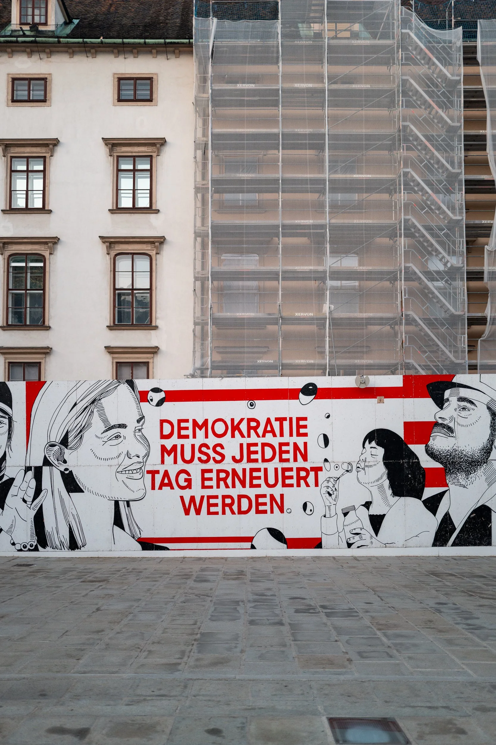 Une affiche murale avec une illustration en noir et blanc de plusieurs personnes, accompagné du texte en allemand "Demokratie muss jeden Tag erneuert werden" en rouge.