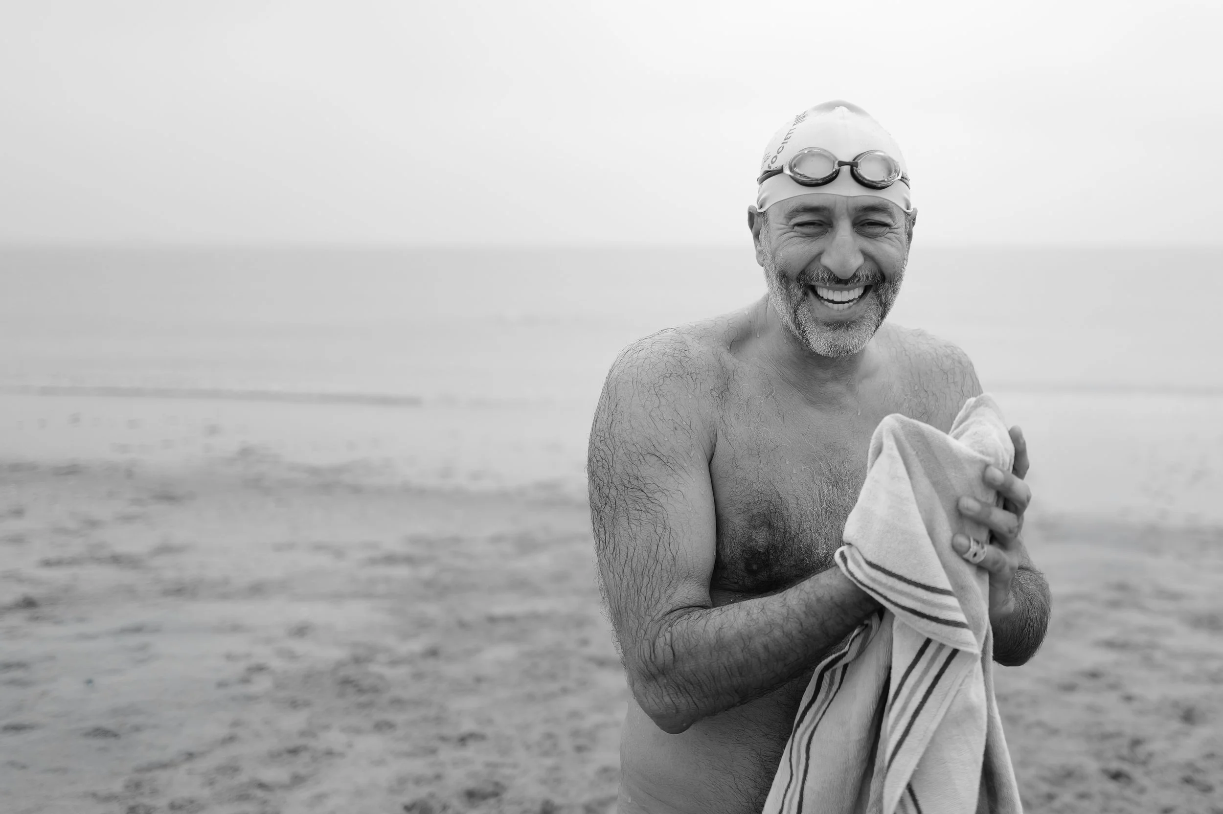Humain souriant portant un bonnet de bain et des lunettes de natation, tenant une serviette dans une plage
