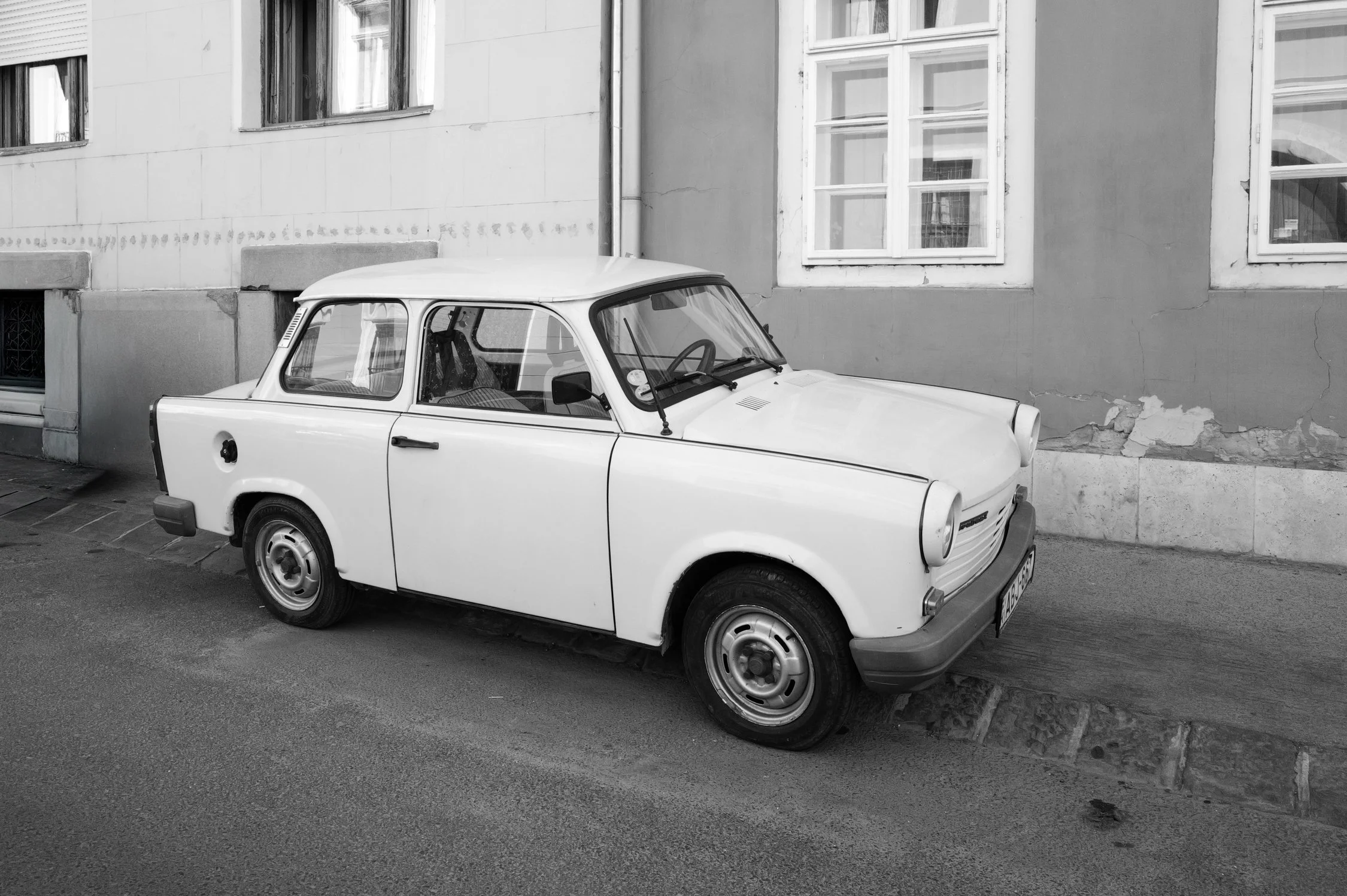 Une voiture blanche ancienne garée devant un immeuble en pierre avec des fenêtres.