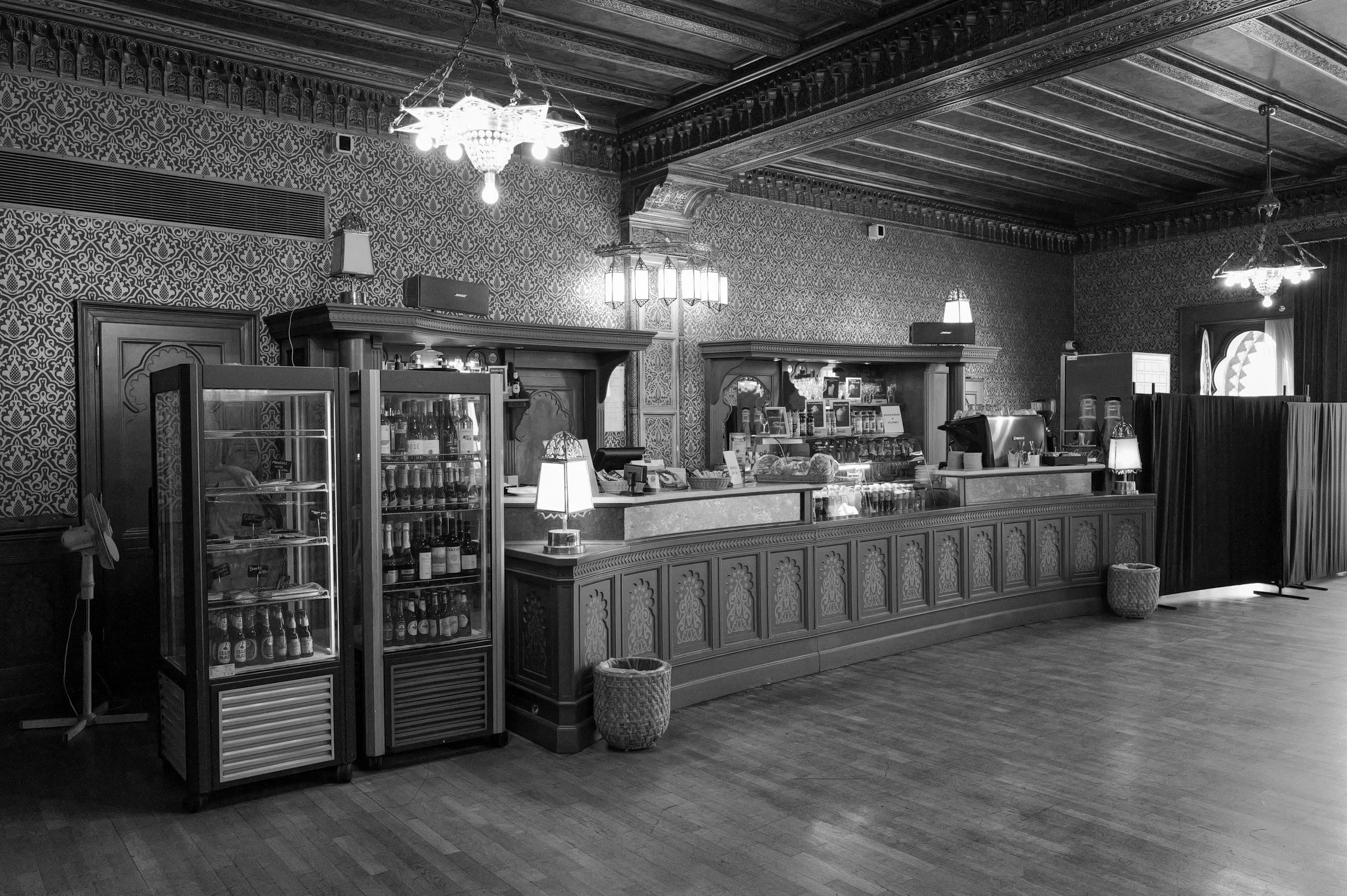Intérieur d'un café ou restaurant avec un comptoir en bois, étagères avec bouteilles, décorations et lampes anciennes, parquet en bois, ambiance vintage.