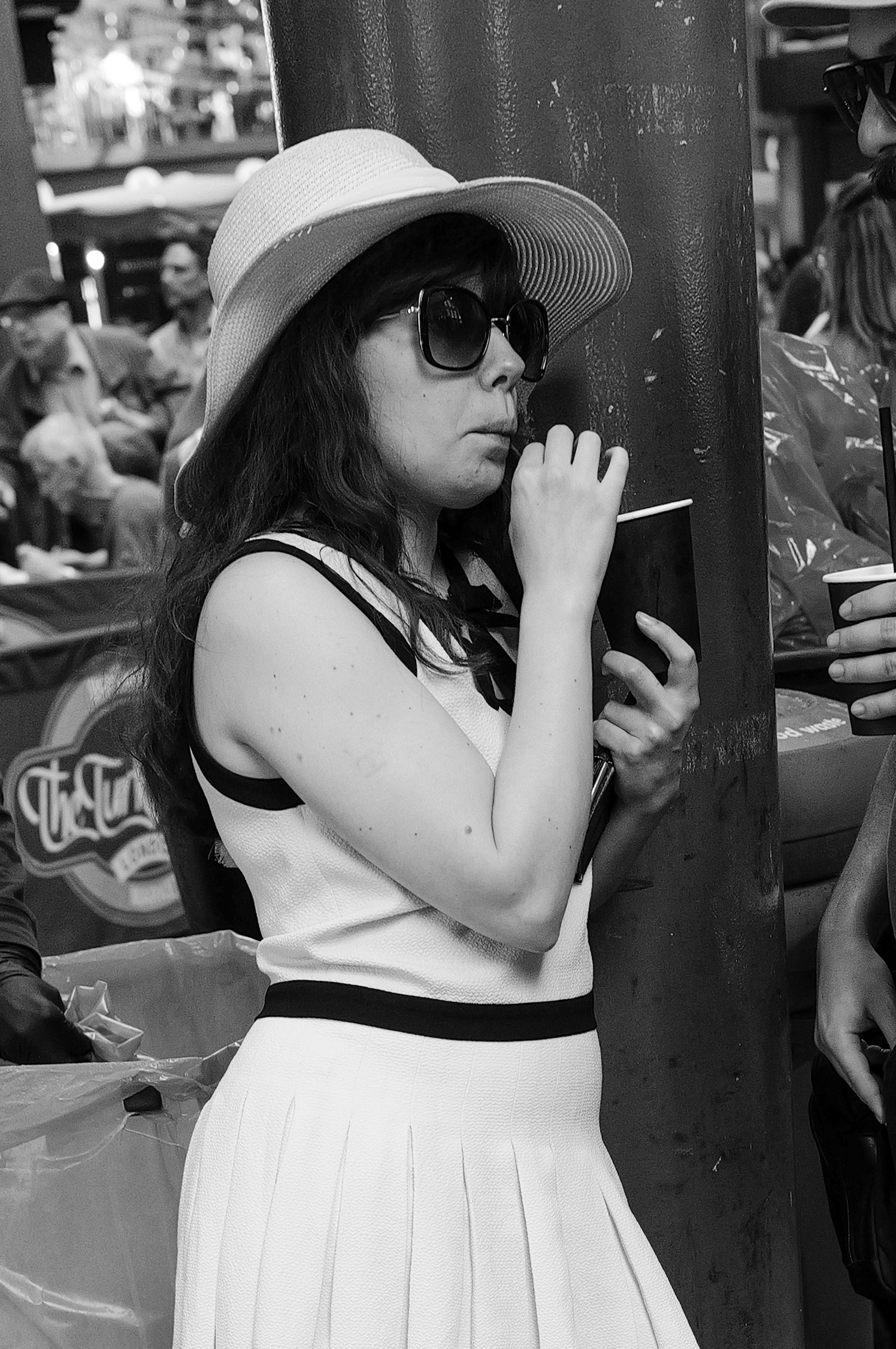 Une femme portant une large panama, des lunettes de soleil et une robe blanche, mais qui fume une cigarette