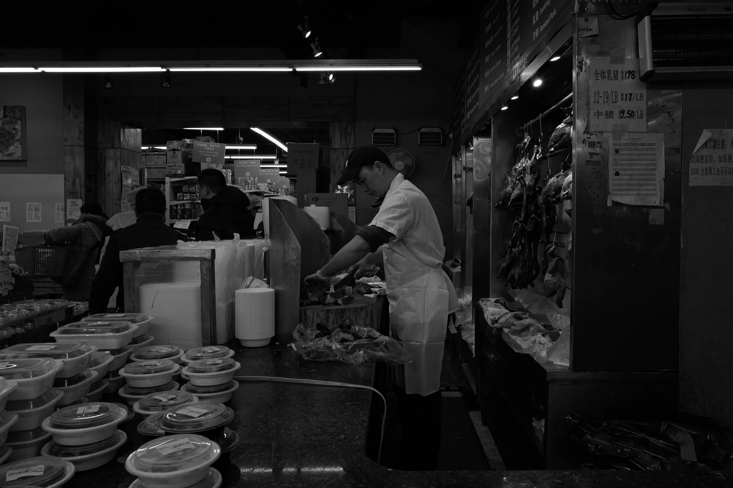 Vendeur de poisson dans une poissonnerie, avec du poisson suspendu derrière lui et des produits emballés sur le comptoir.