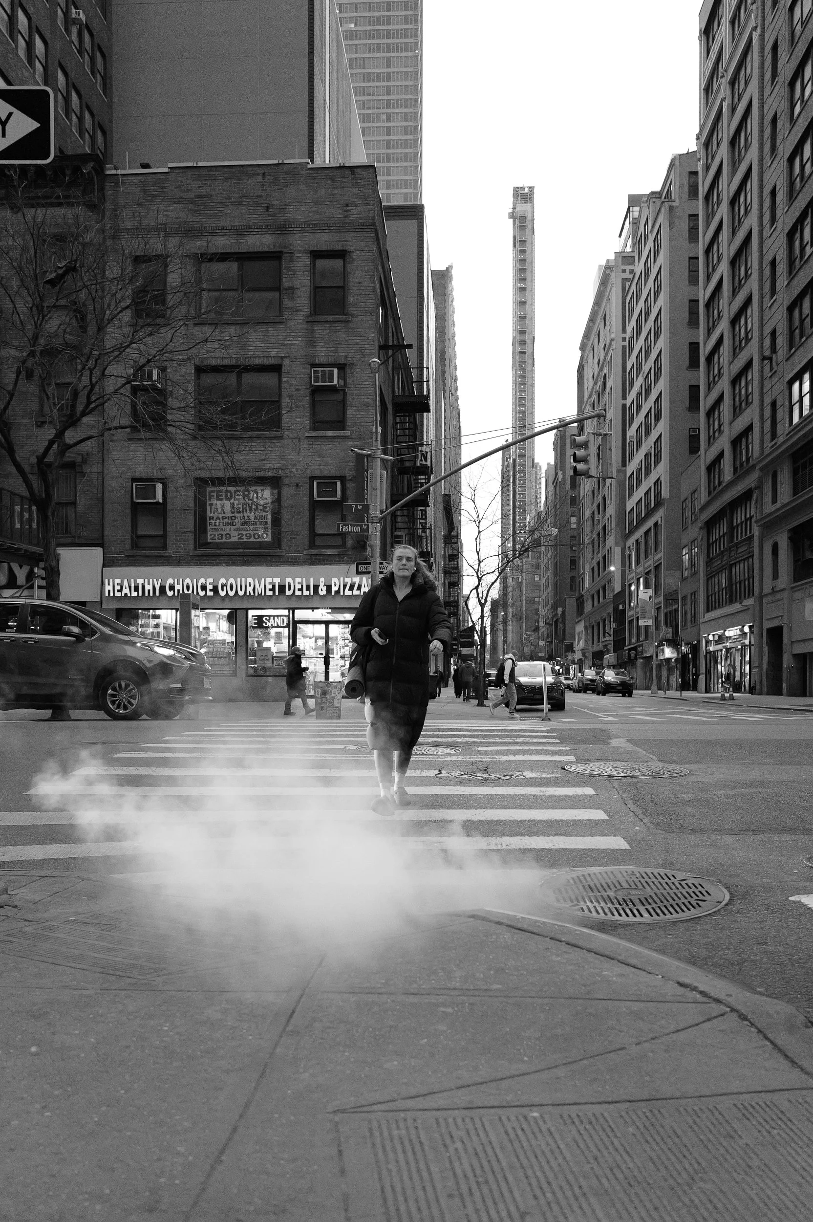 Une femme traverse un passage piéton dans une ville urbaine, avec des immeubles en arrière-plan, dans une ambiance en noir et blanc.
