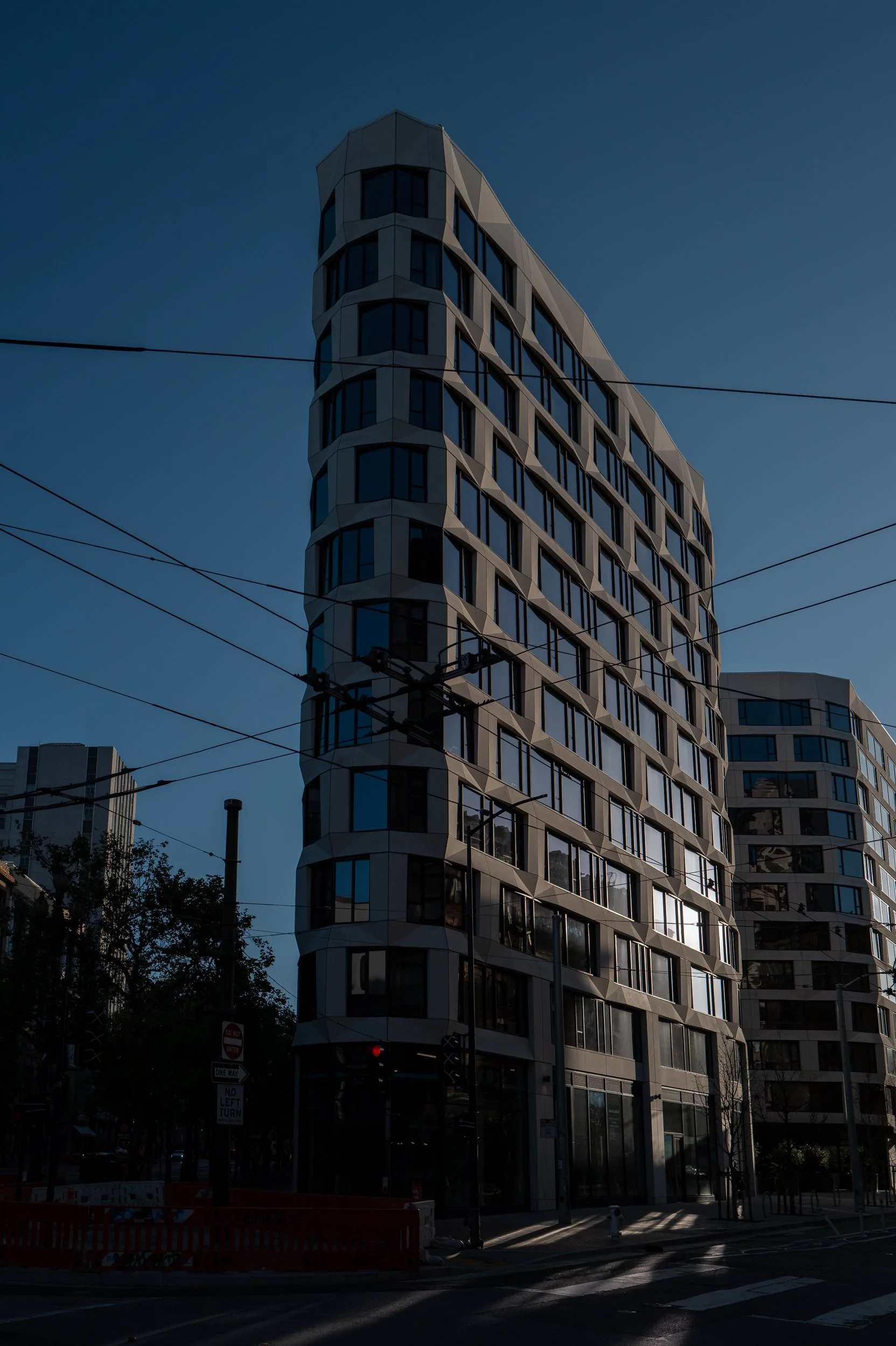 Immeuble moderne avec des fenêtres arrondies, vu dans un ciel clair, avec des lignes électriques en premier plan.